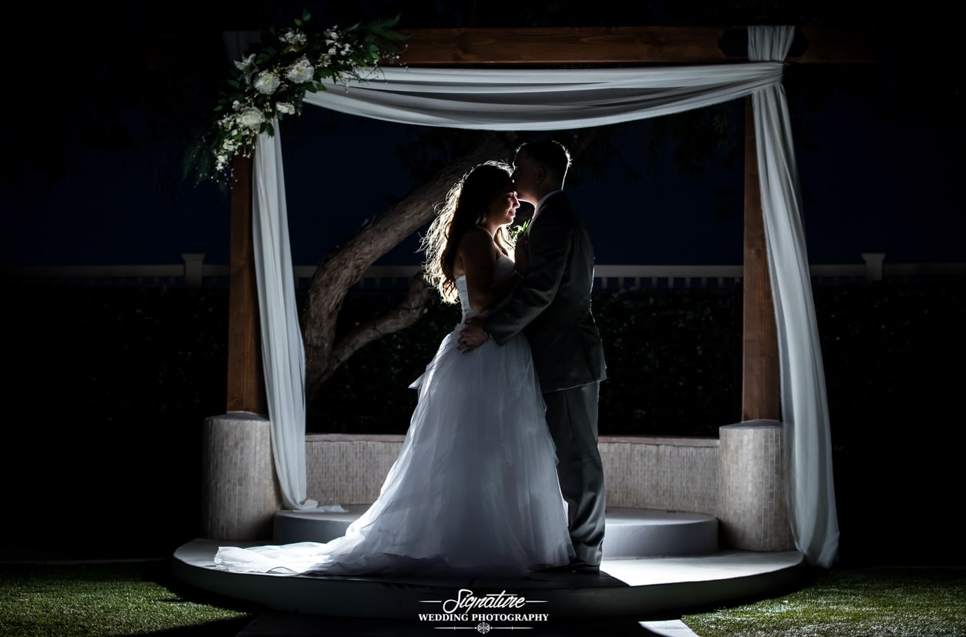 Groom kissing bride's forehead under archway silhouette