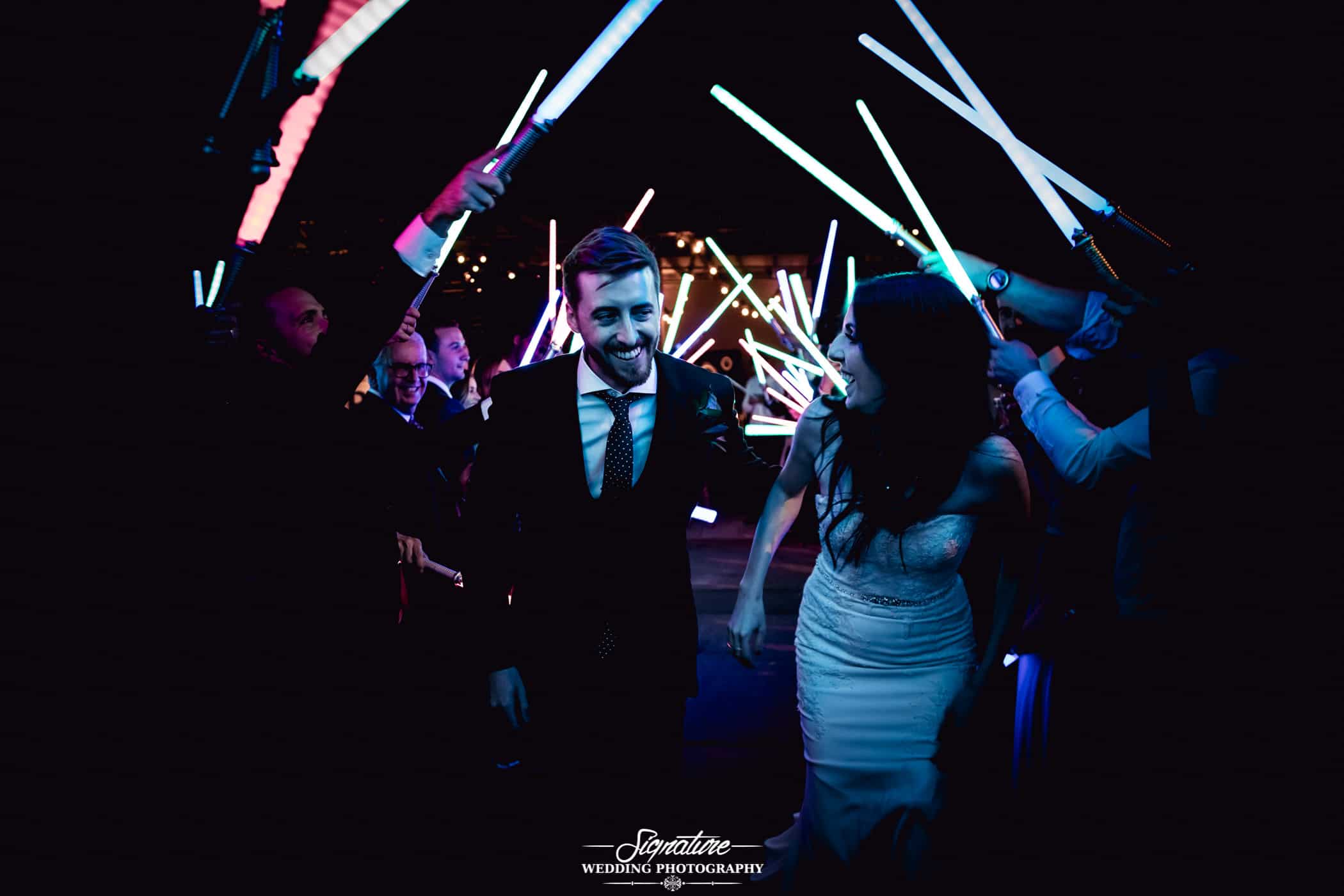 Bride and groom walking under lightsaber tunnel
