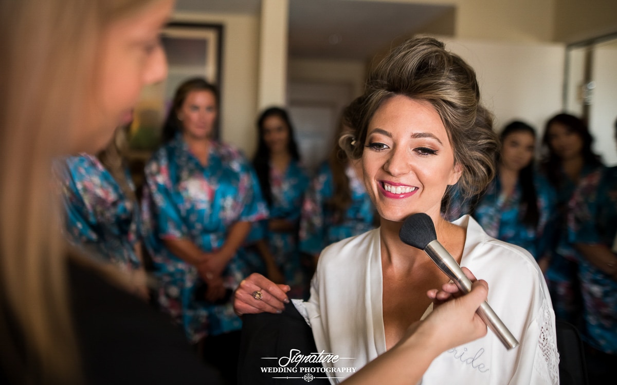Bride getting makeup done with bridesmaids in background