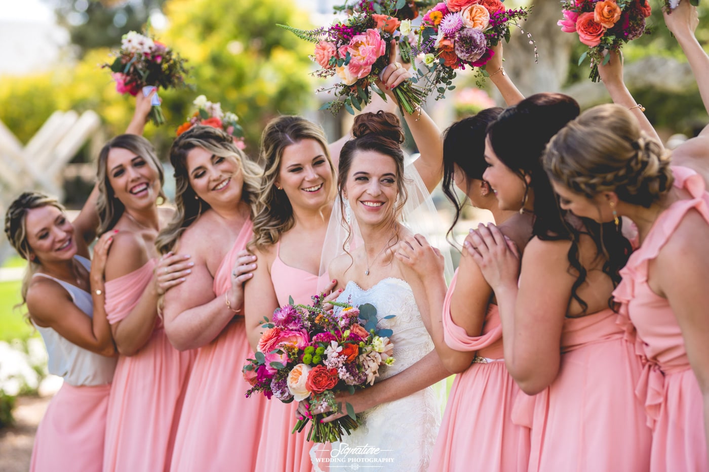 Bridesmaids raising bouquets smiling at bride