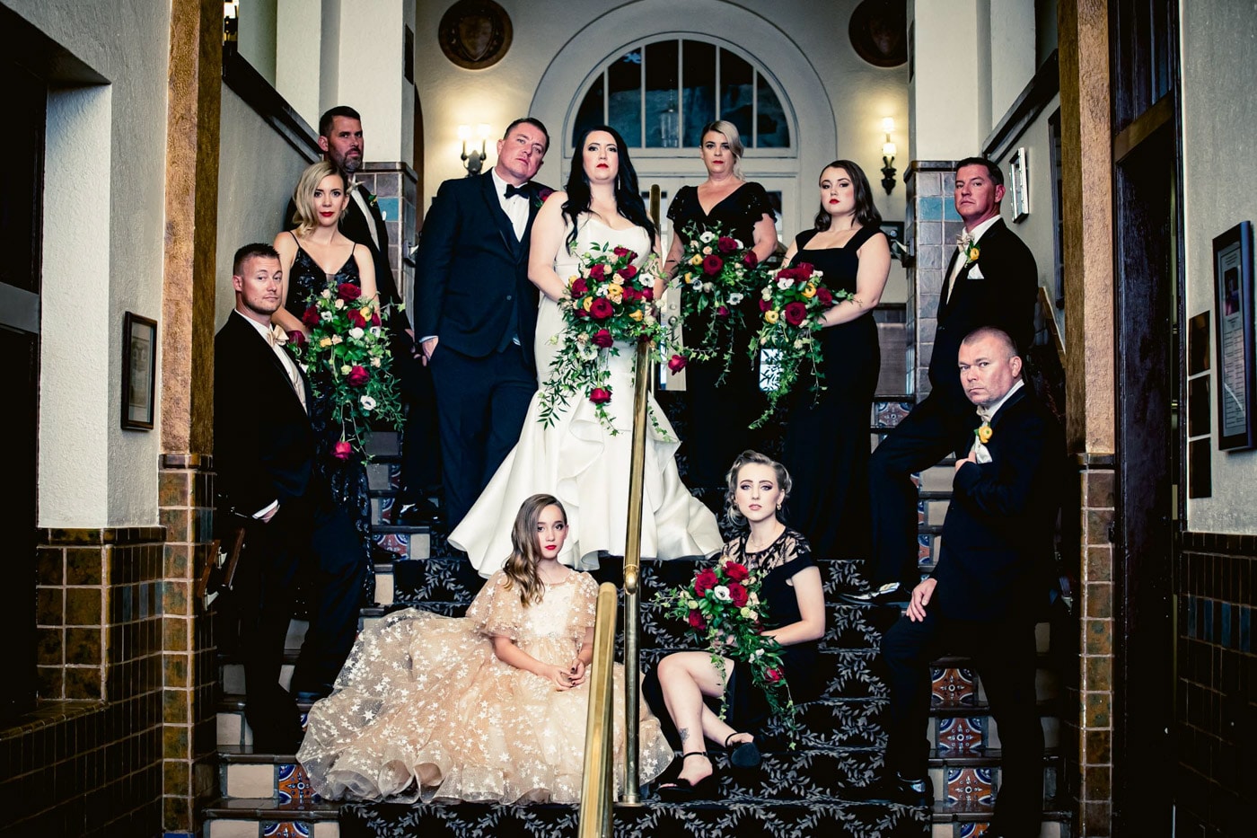 Bride and groom poses on stairs with wedding party