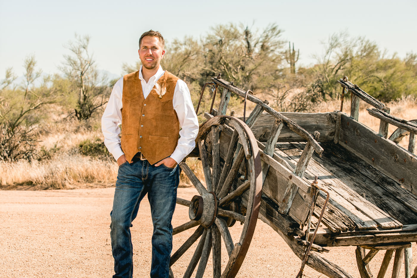 Groom smiling in front of antique wagon in desert