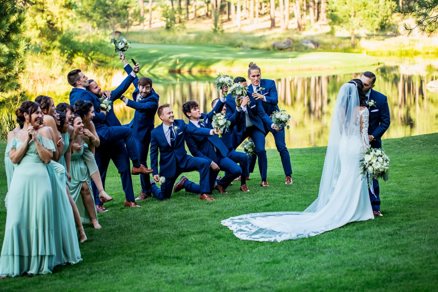 Bride and groom kiss with wedding party in funny poses behind