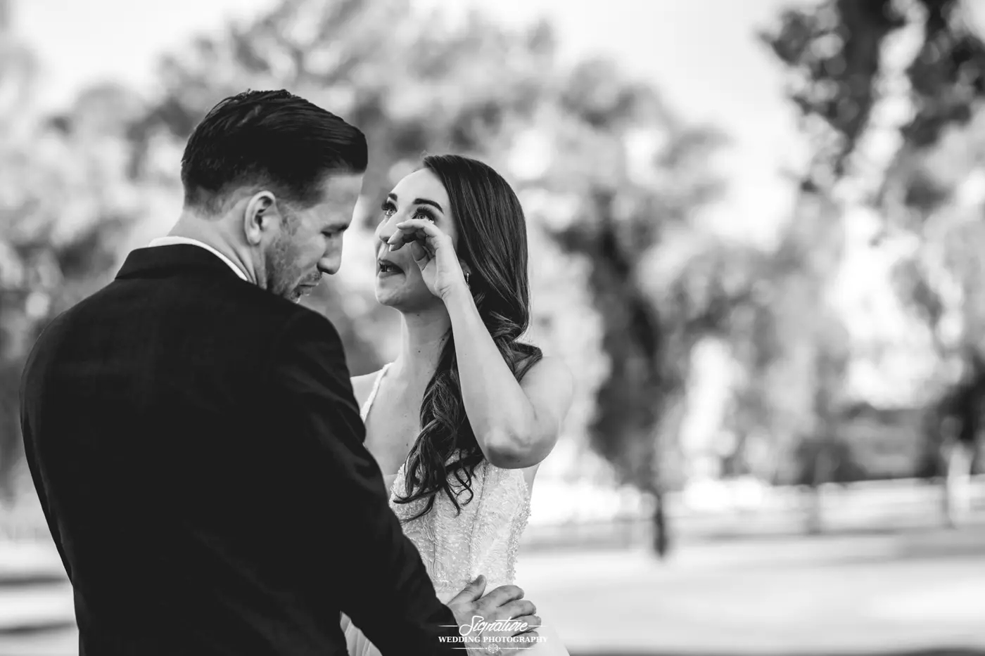 Bride wiping tear groom holds her waist black and white