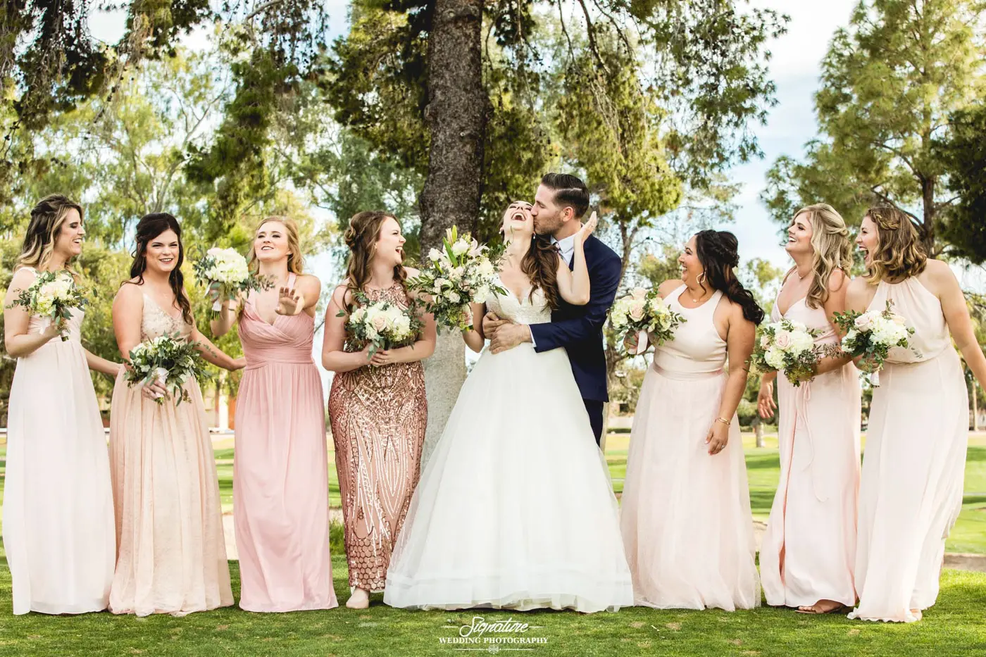 Groom kissing bride on cheek with bridesmaids