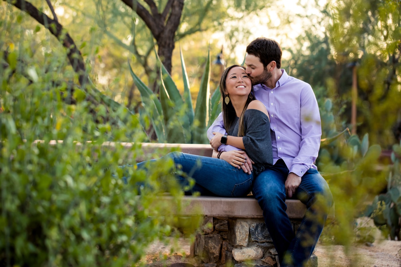 Man kissing woman on cheek sitting on bench with desert plants