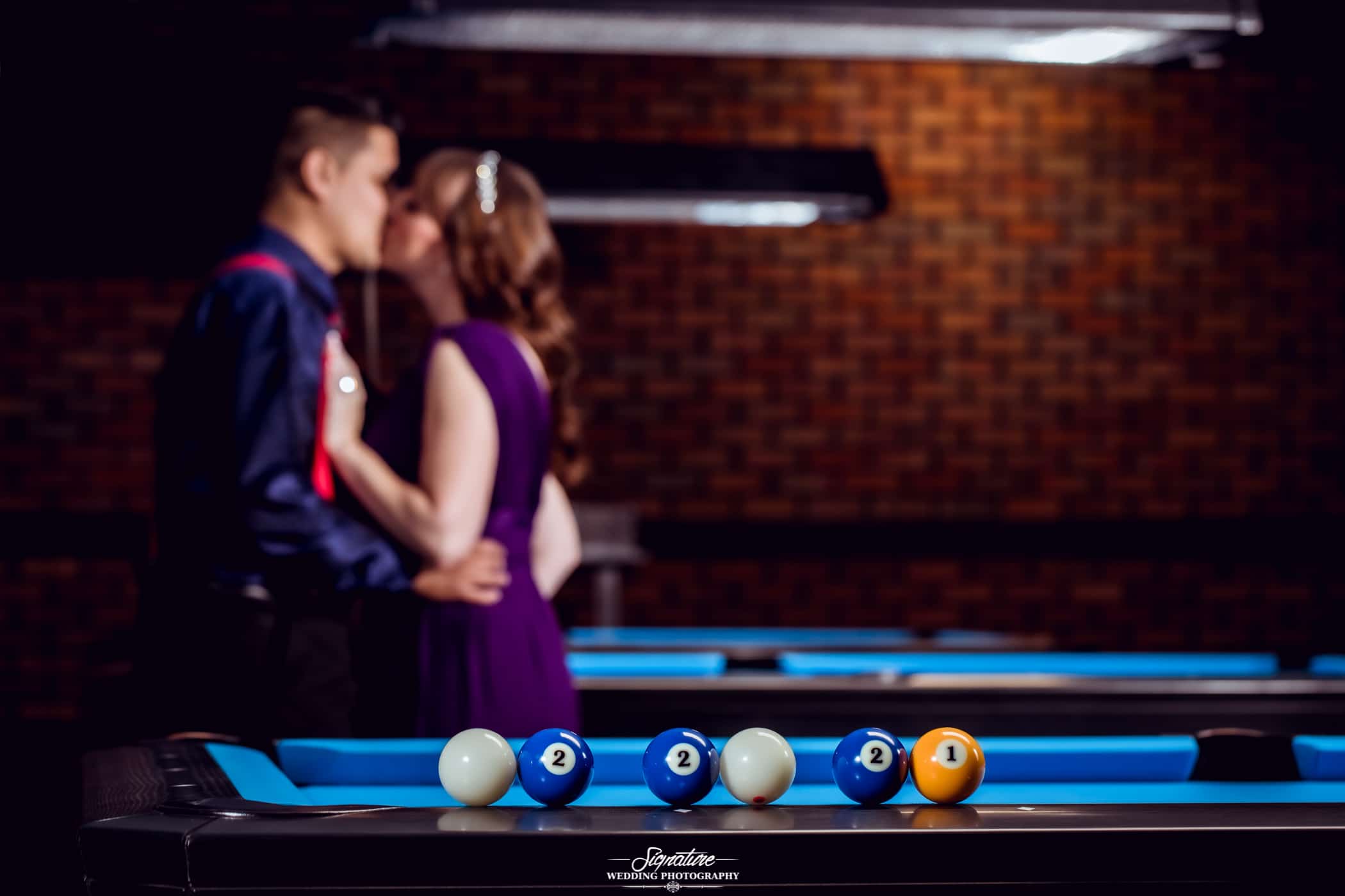 Couple kissing behind billiards table with date on billiard balls