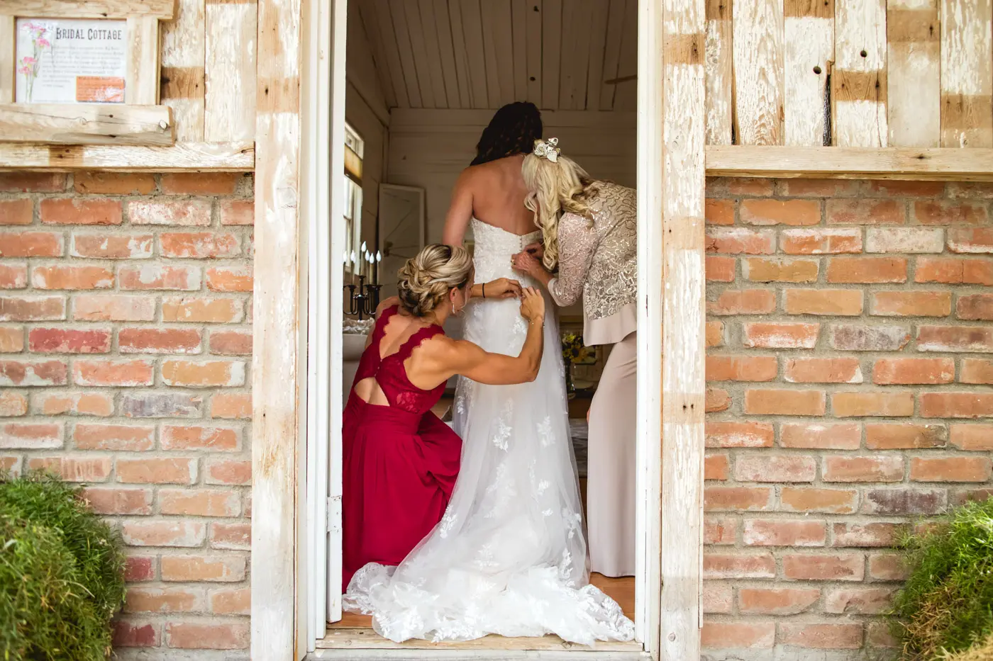 Matriarch and bridesmaid fastening up bride's dress