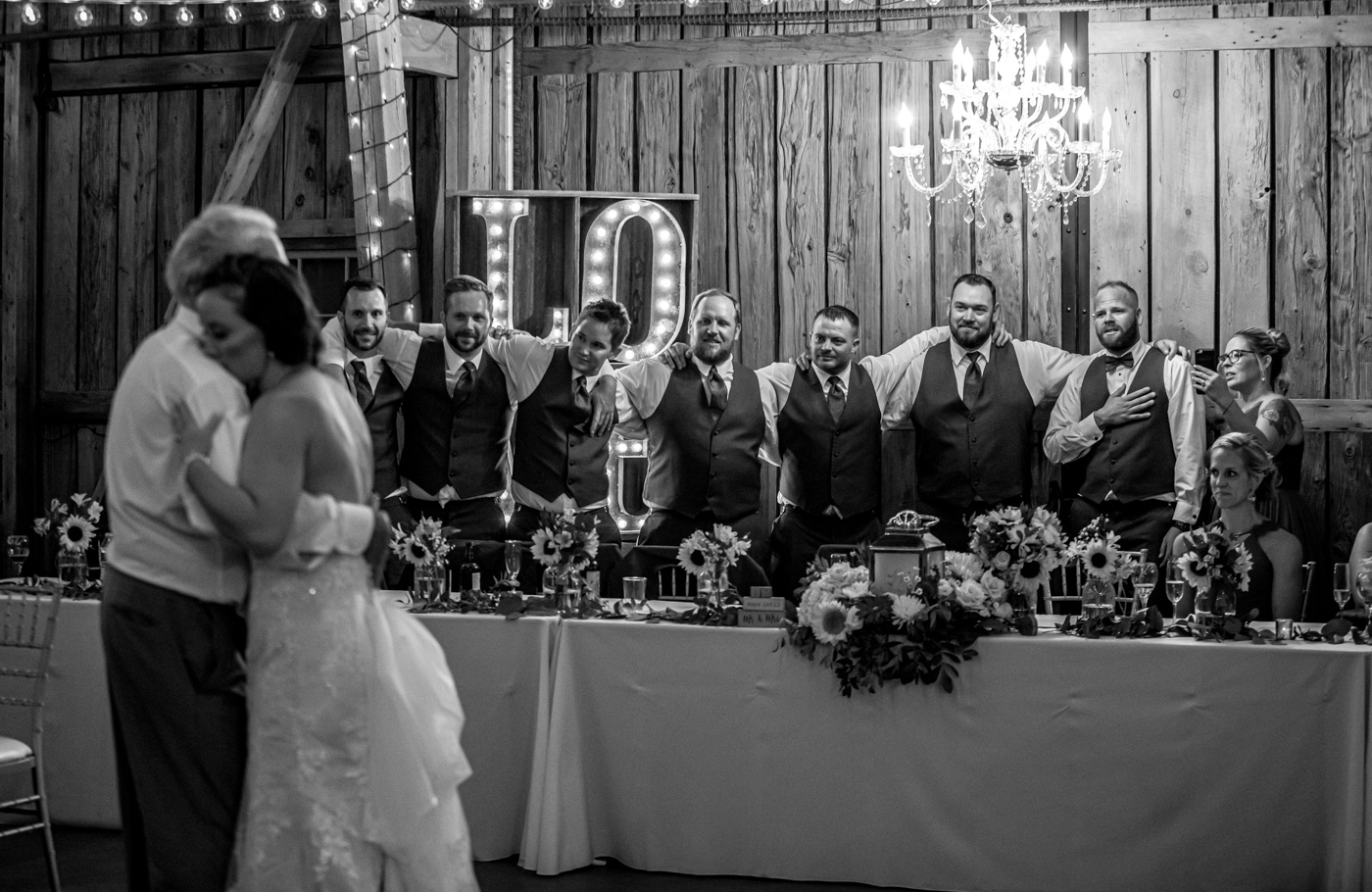 Groom and groomsmen watching bride and father dance black and white