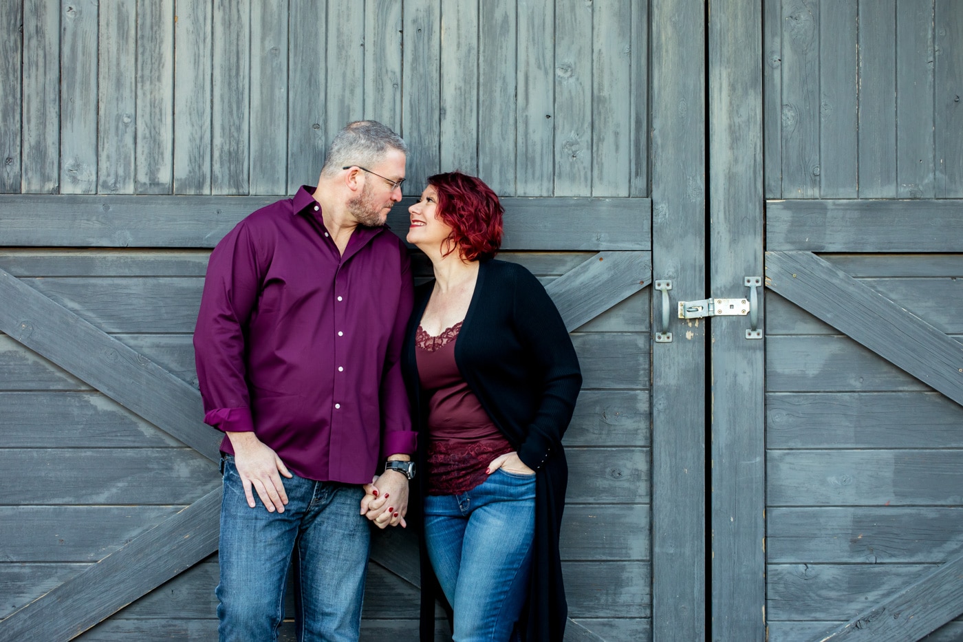 Couple holding hands looking at each other in front of barn doors