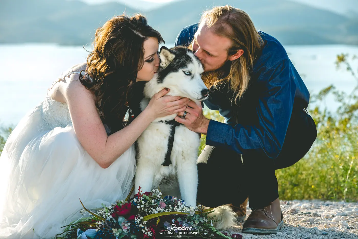 Bride and groom knelt down kissing dog