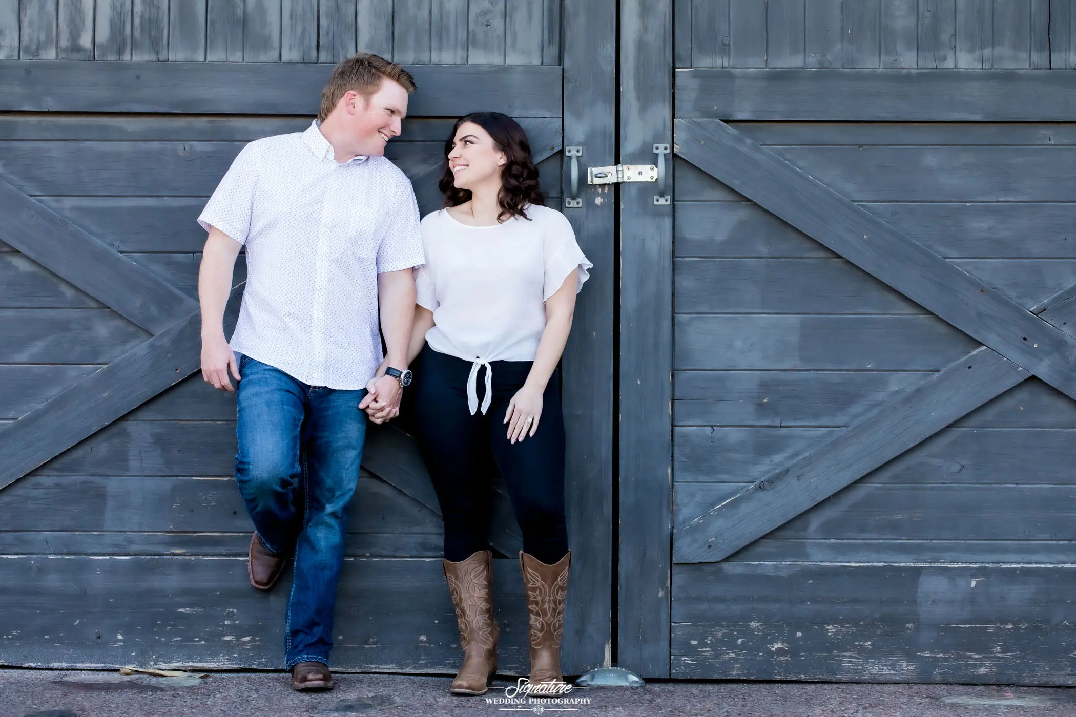 Couple holding hands looking at each other in front of barn doors