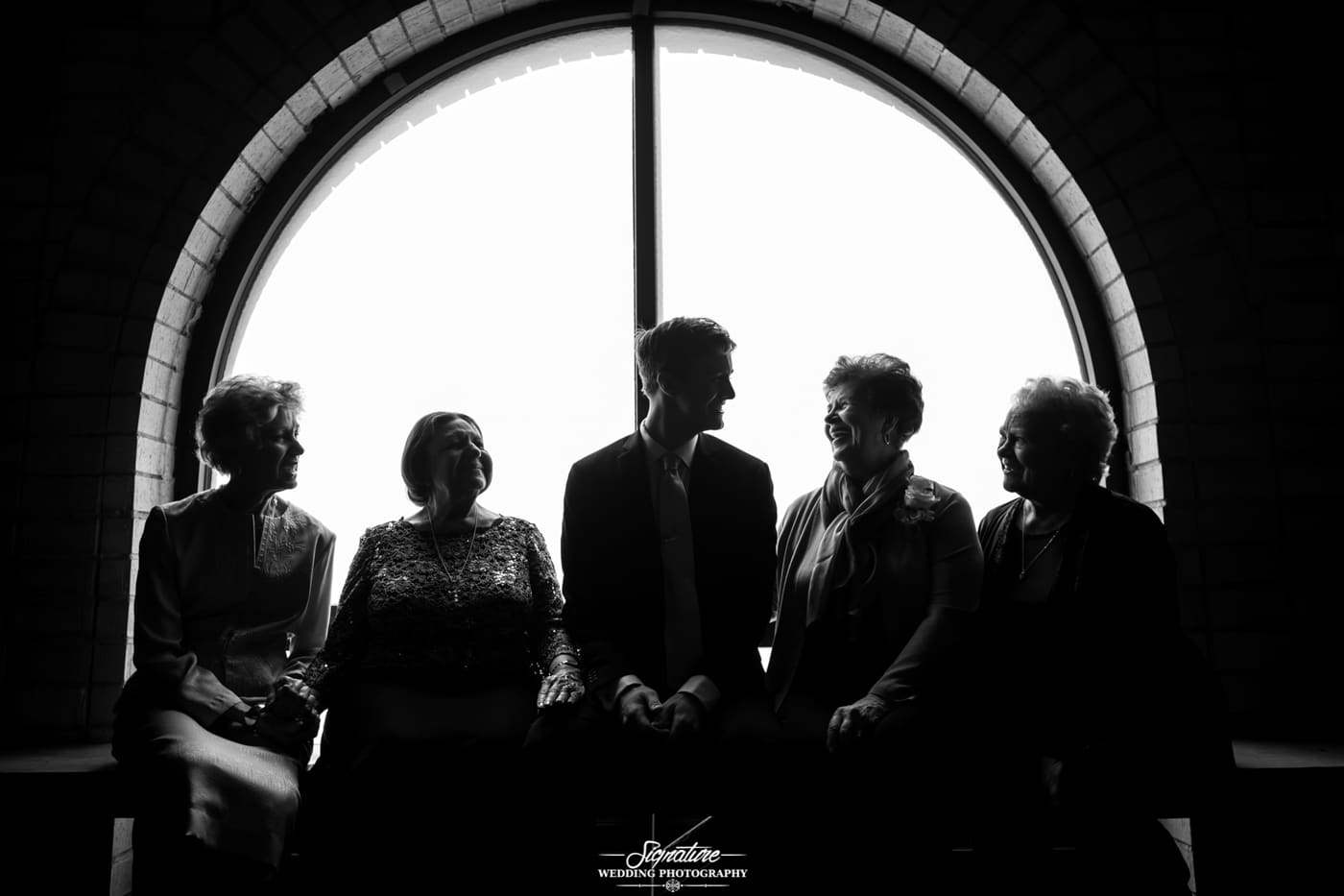 Groom with matriarch sitting in front of window silhouette black and white