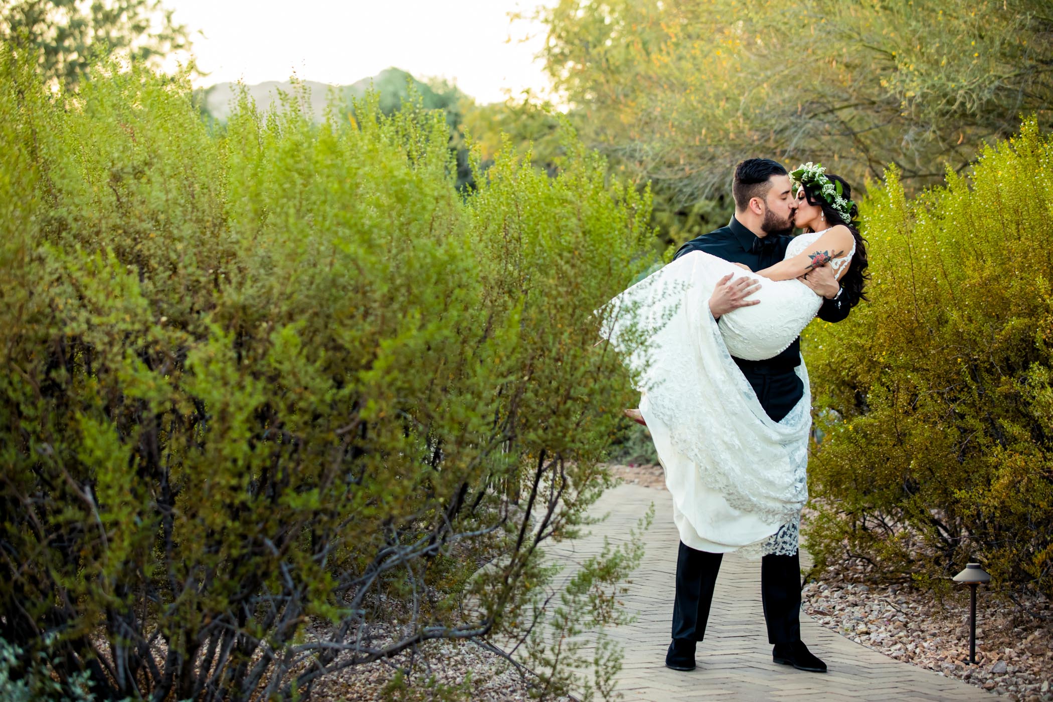 Groom picking up bride and kissing on desert path