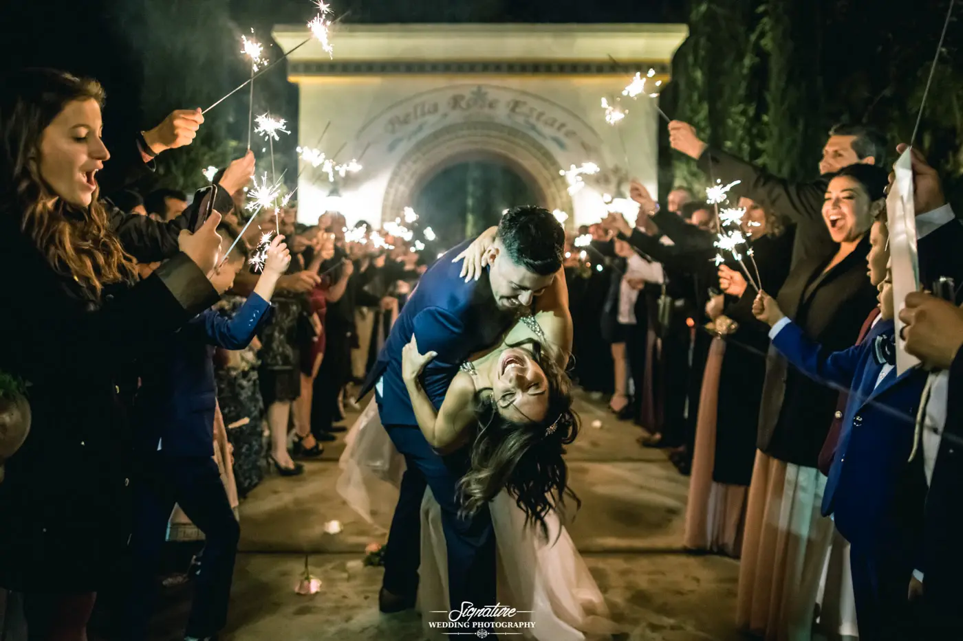 Groom dipping bride with wedding guests holding sparklers