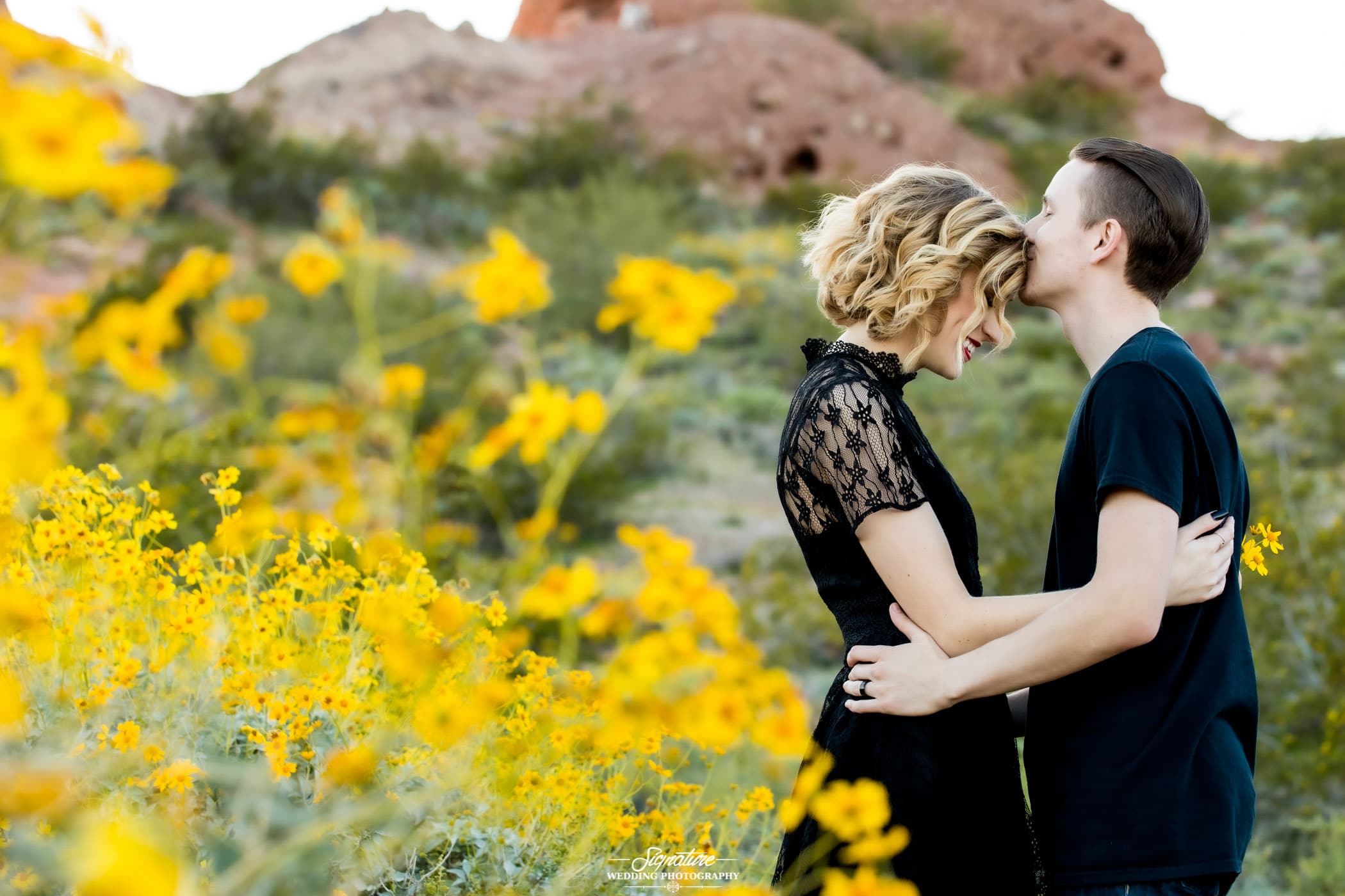 Man kissing woman on forehead with desert flowers