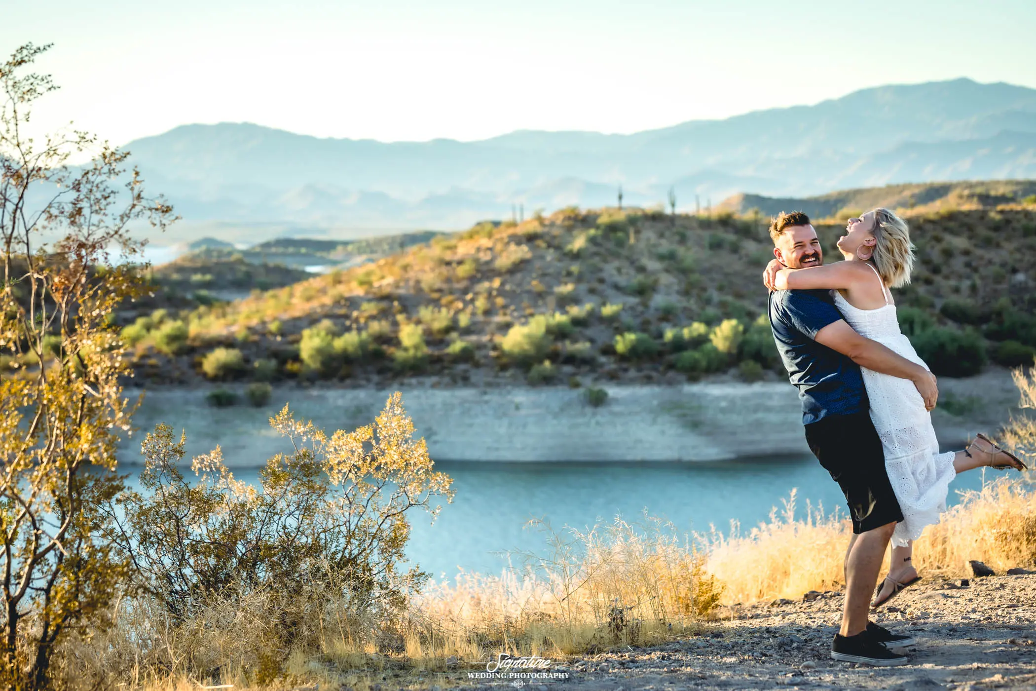 Man picking up woman laughing in front of lake