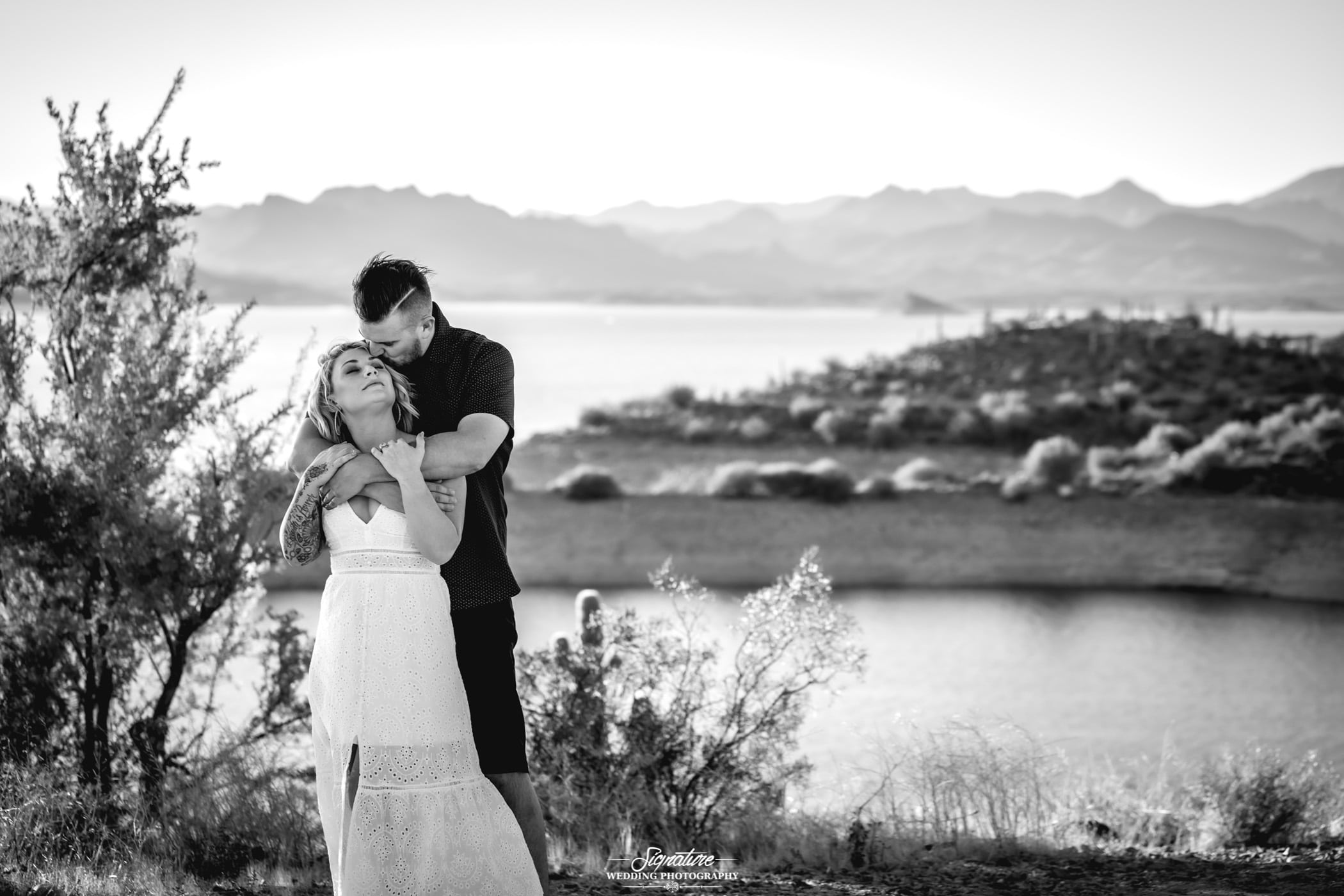 Man hugging woman from behind in front of lake in desert black and white