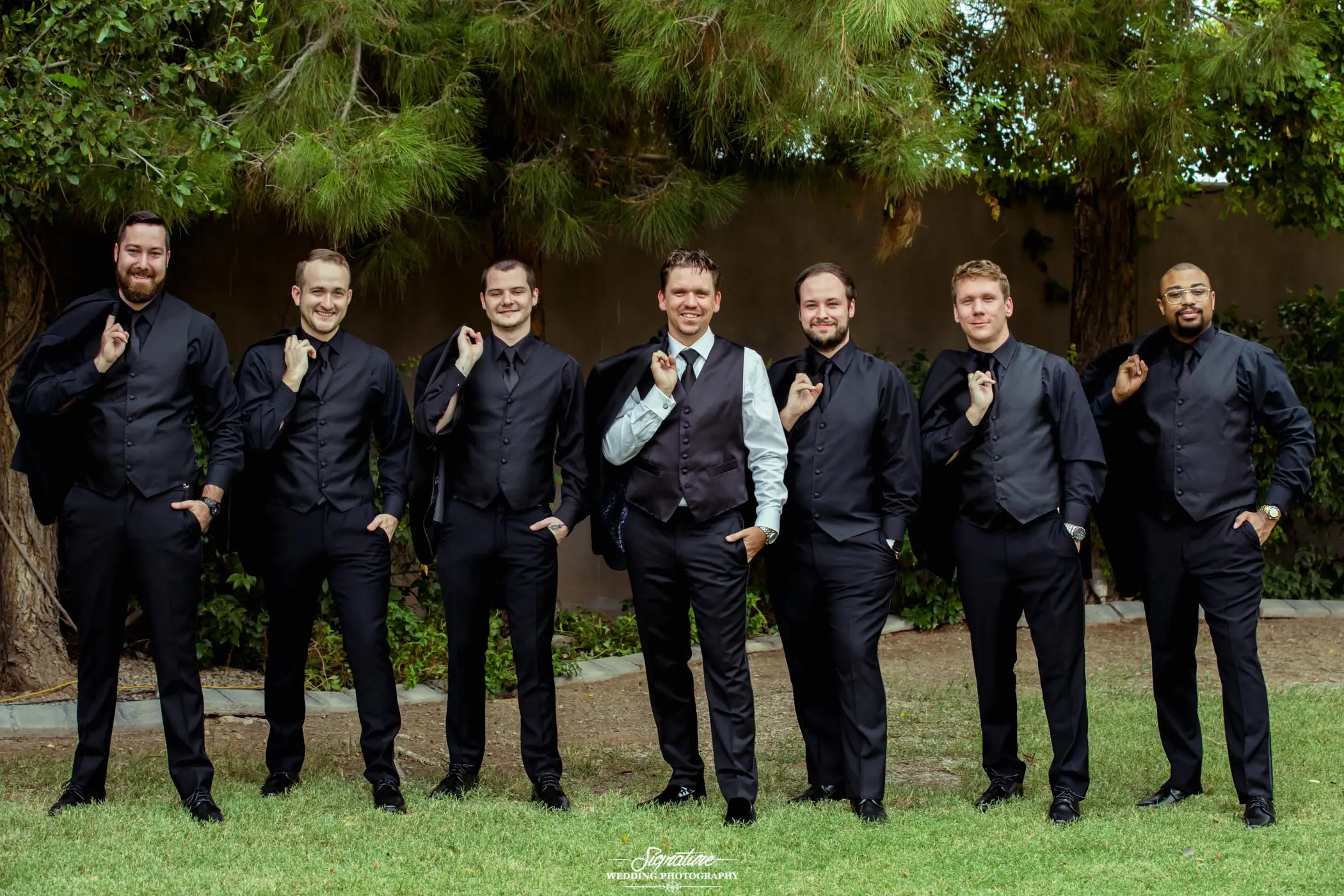 Groom and groomsmen holding jackets in arms smiling at camera