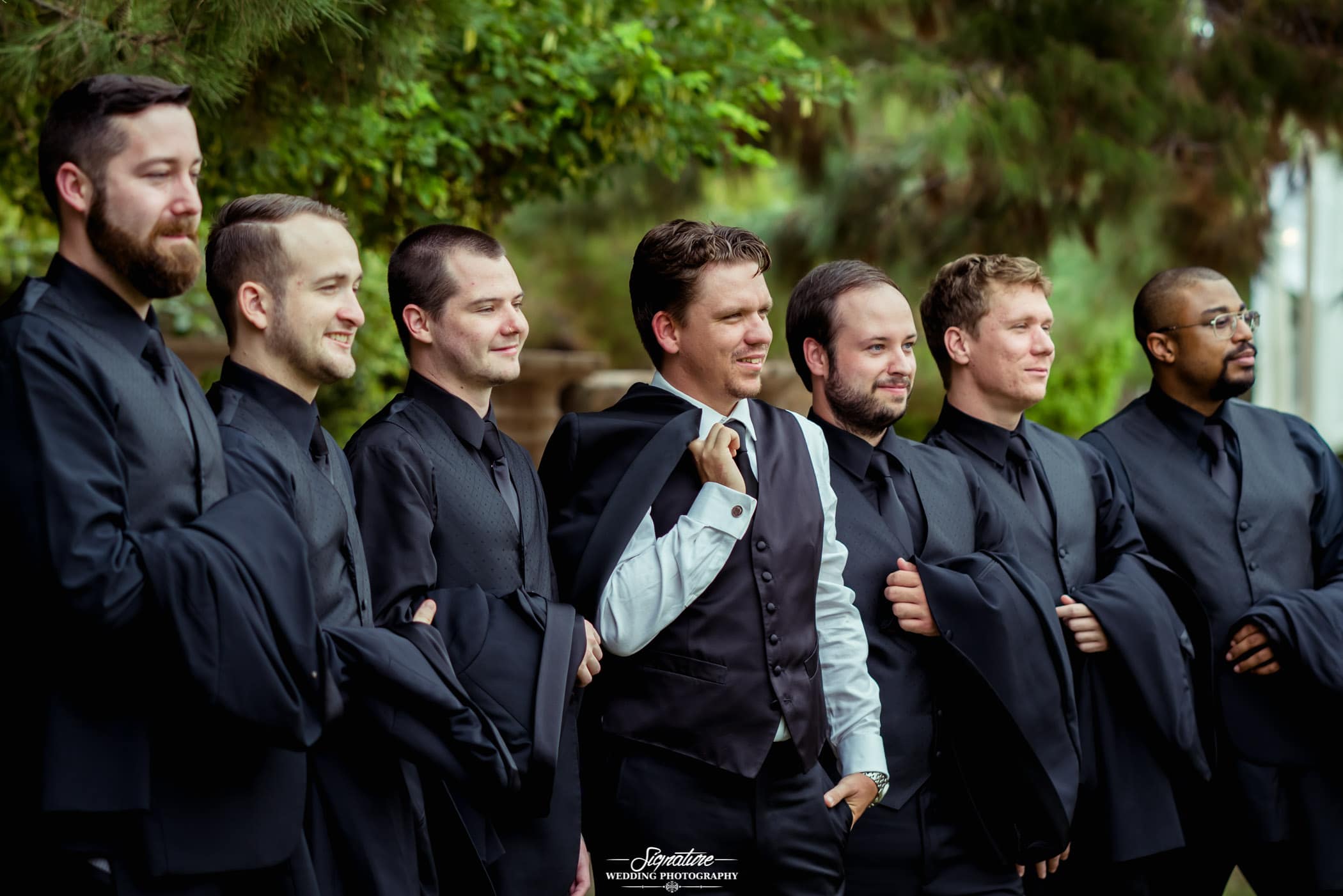 Groom and groomsmen holding jackets in arms