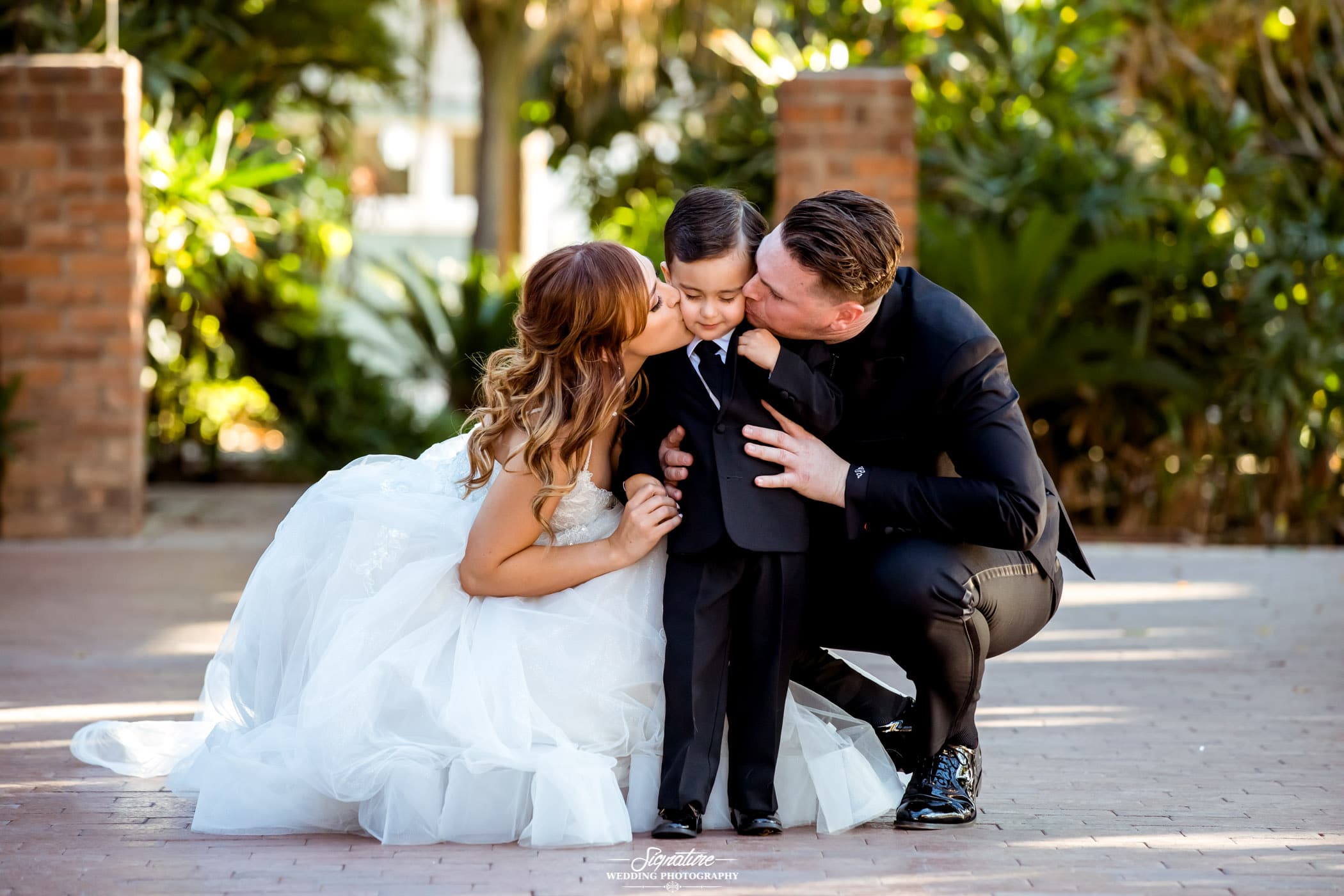 Bride and groom bent down kissing child on cheeks