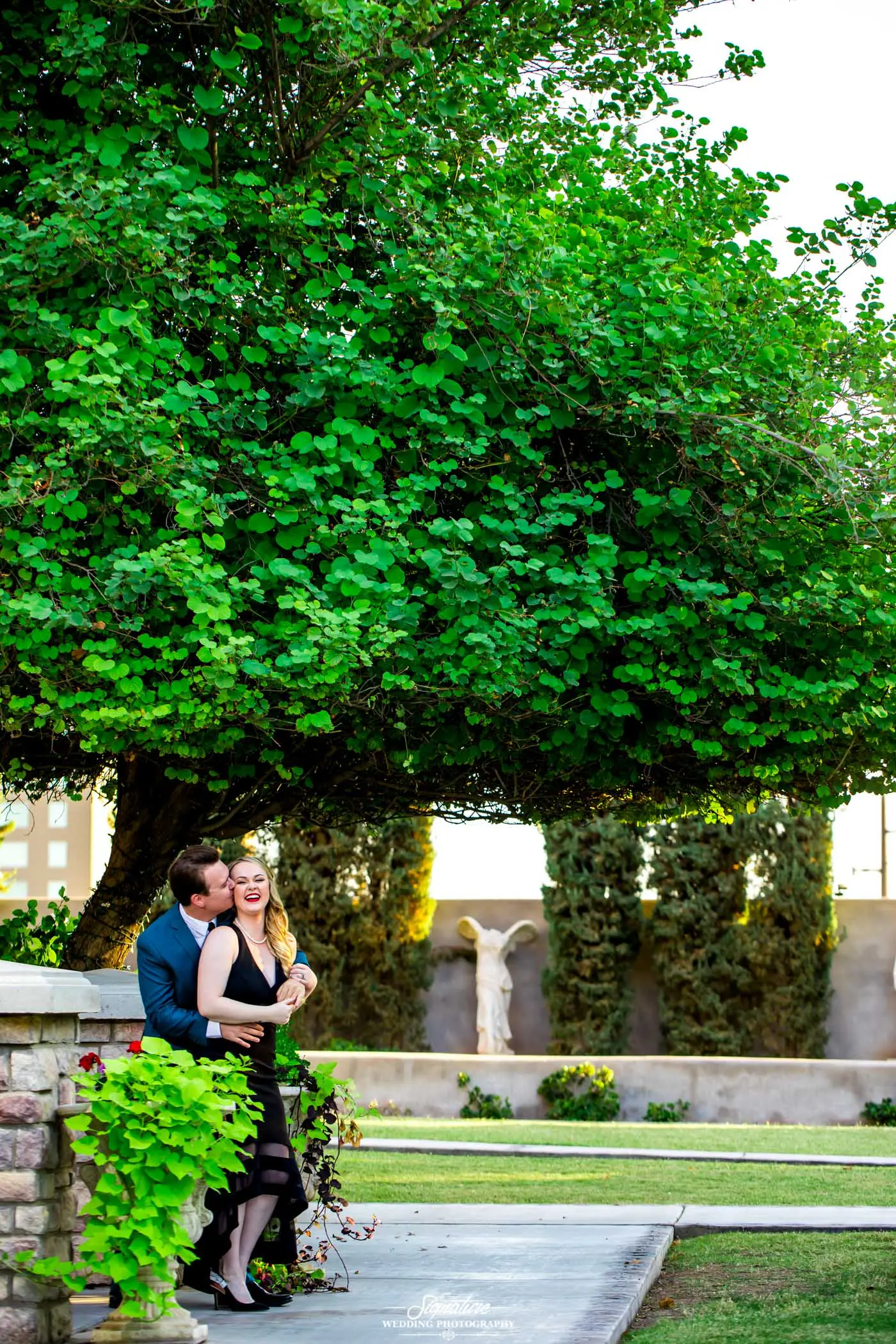 Man kissing woman on cheek under tree