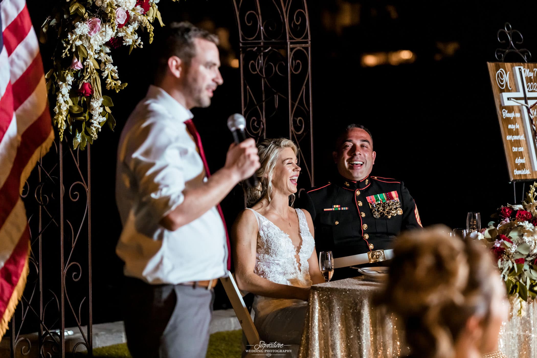 Bride and groom laughing while man gives speech