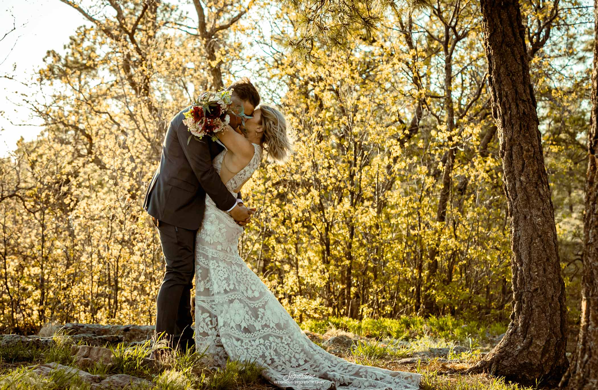 Bride and groom kissing in front of trees