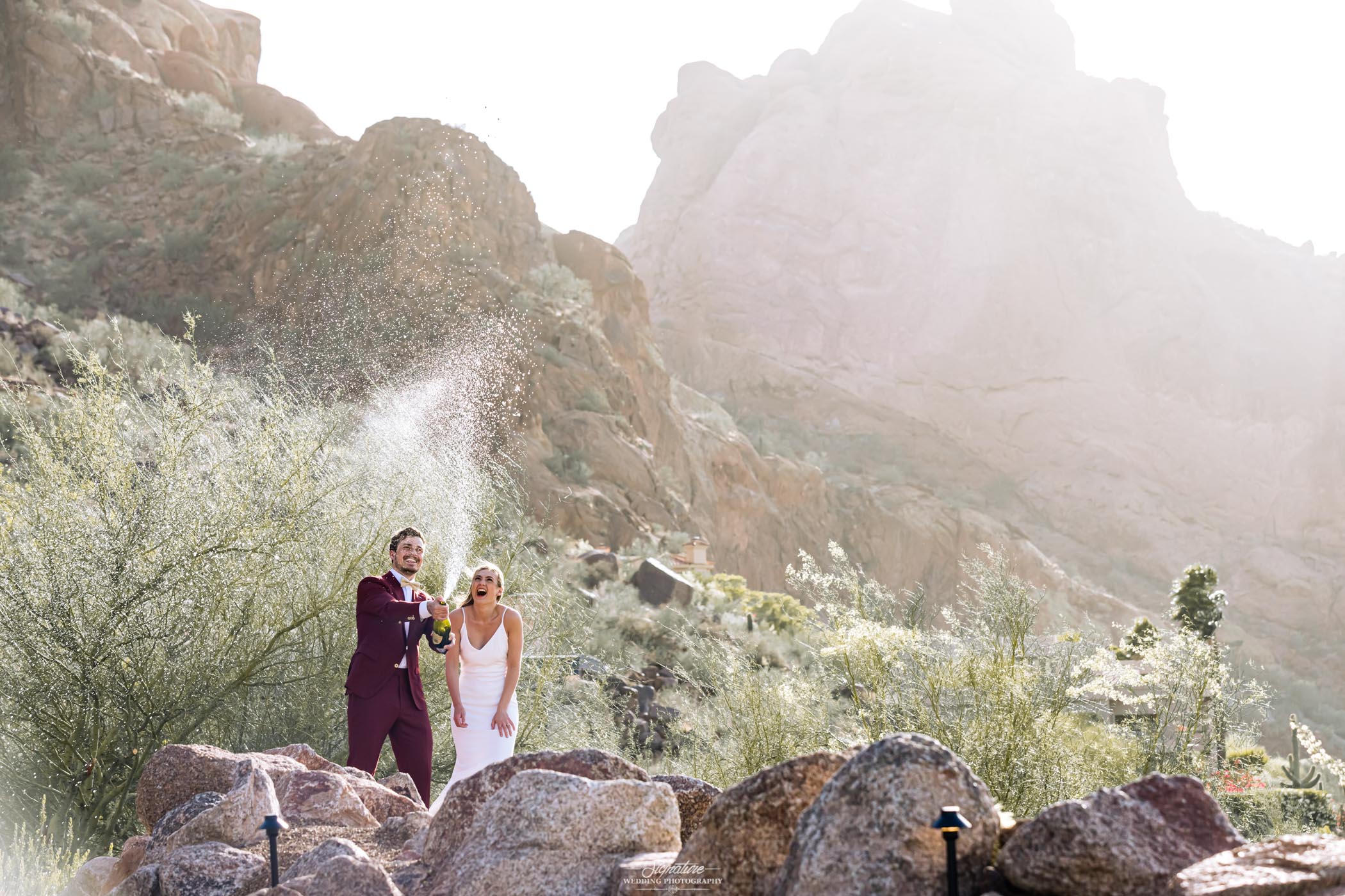 Groom spraying champagne with bride in desert