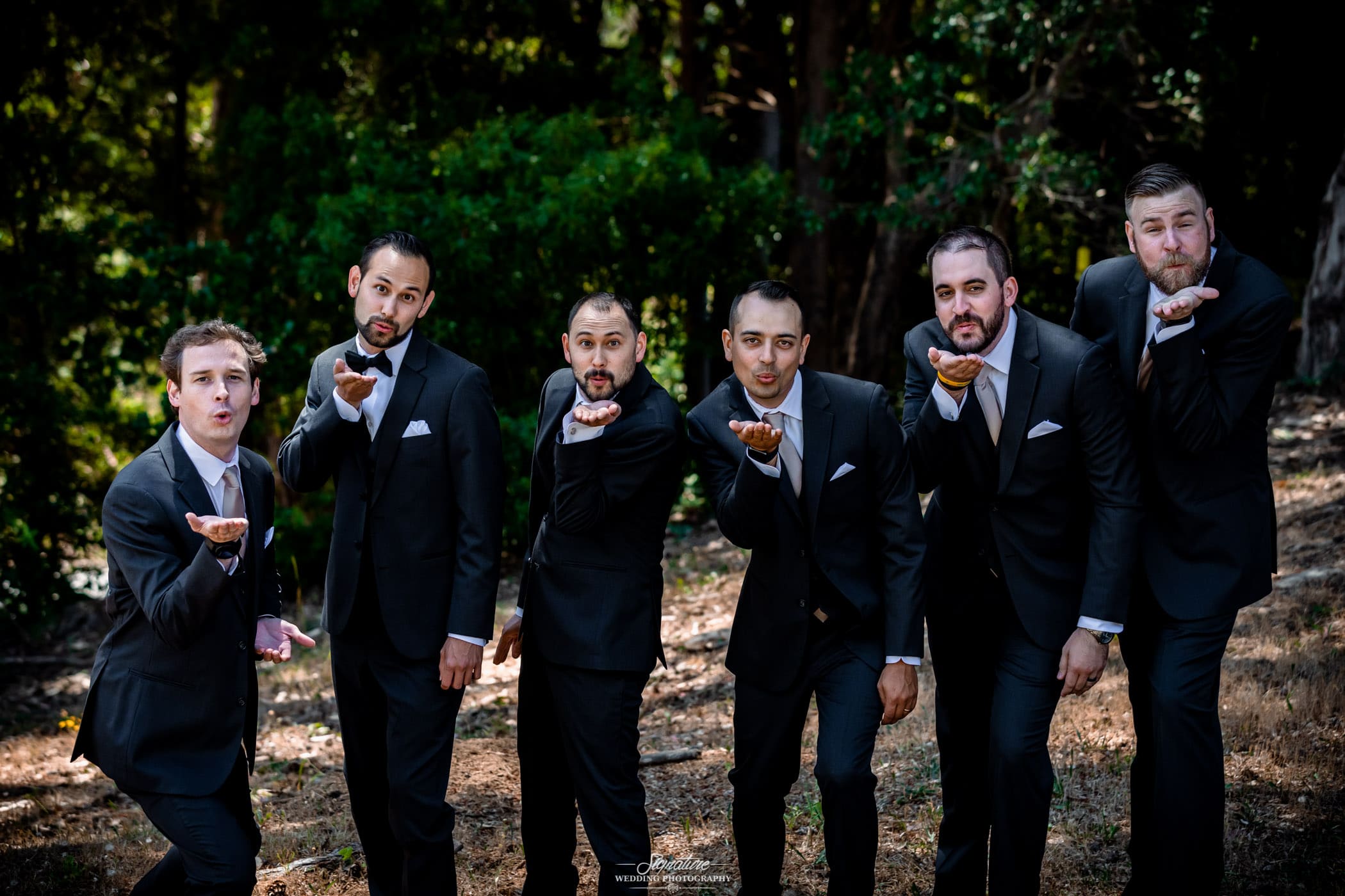 Groom and groomsmen blow kiss in forest