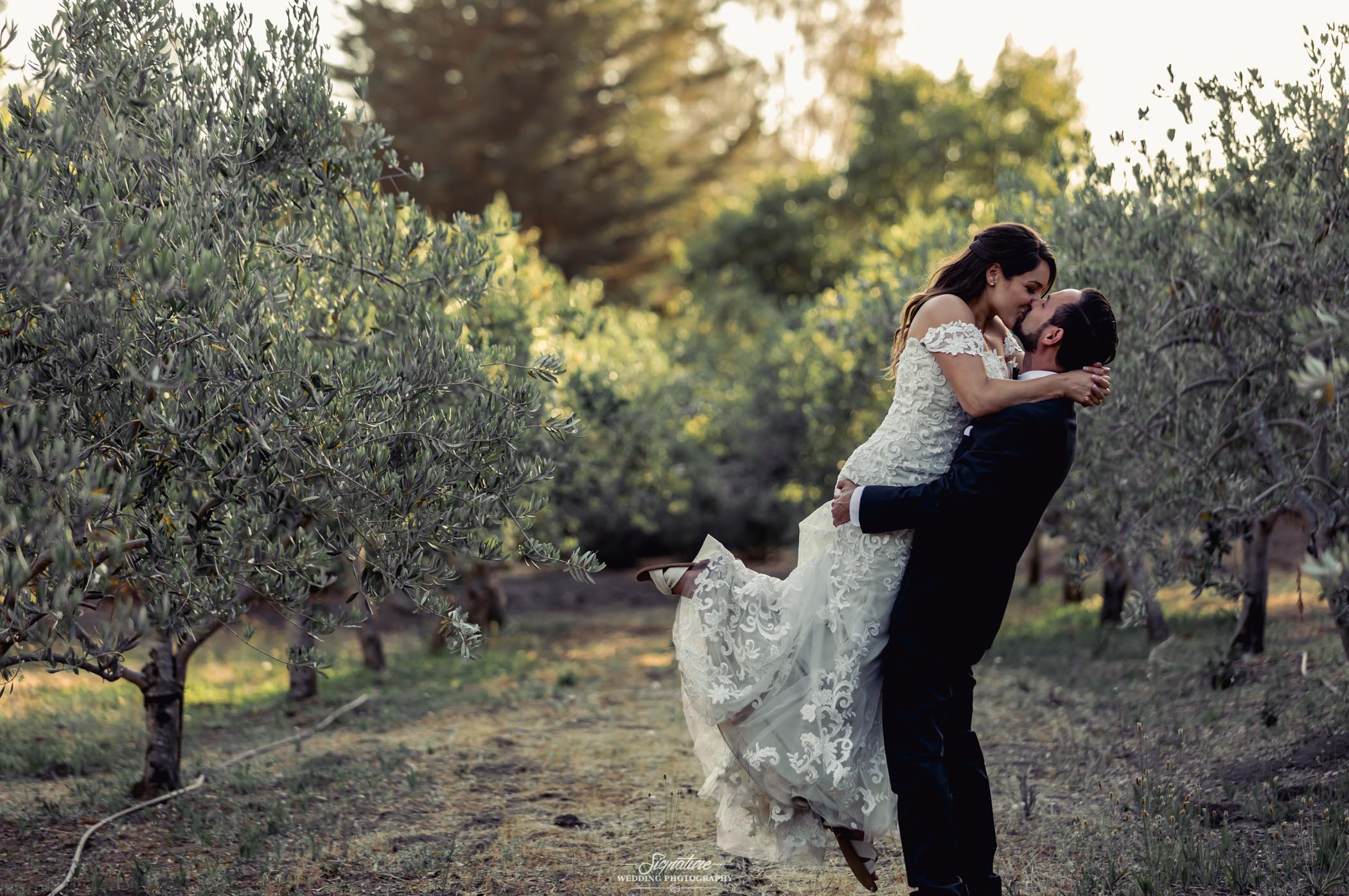 Groom picking up bride and kissing within trees