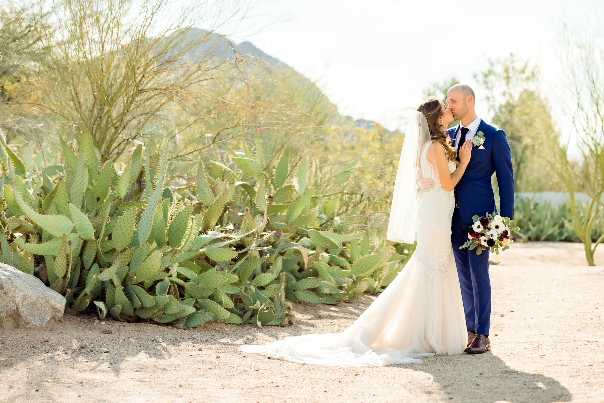 Bride and groom kissing next to cacti