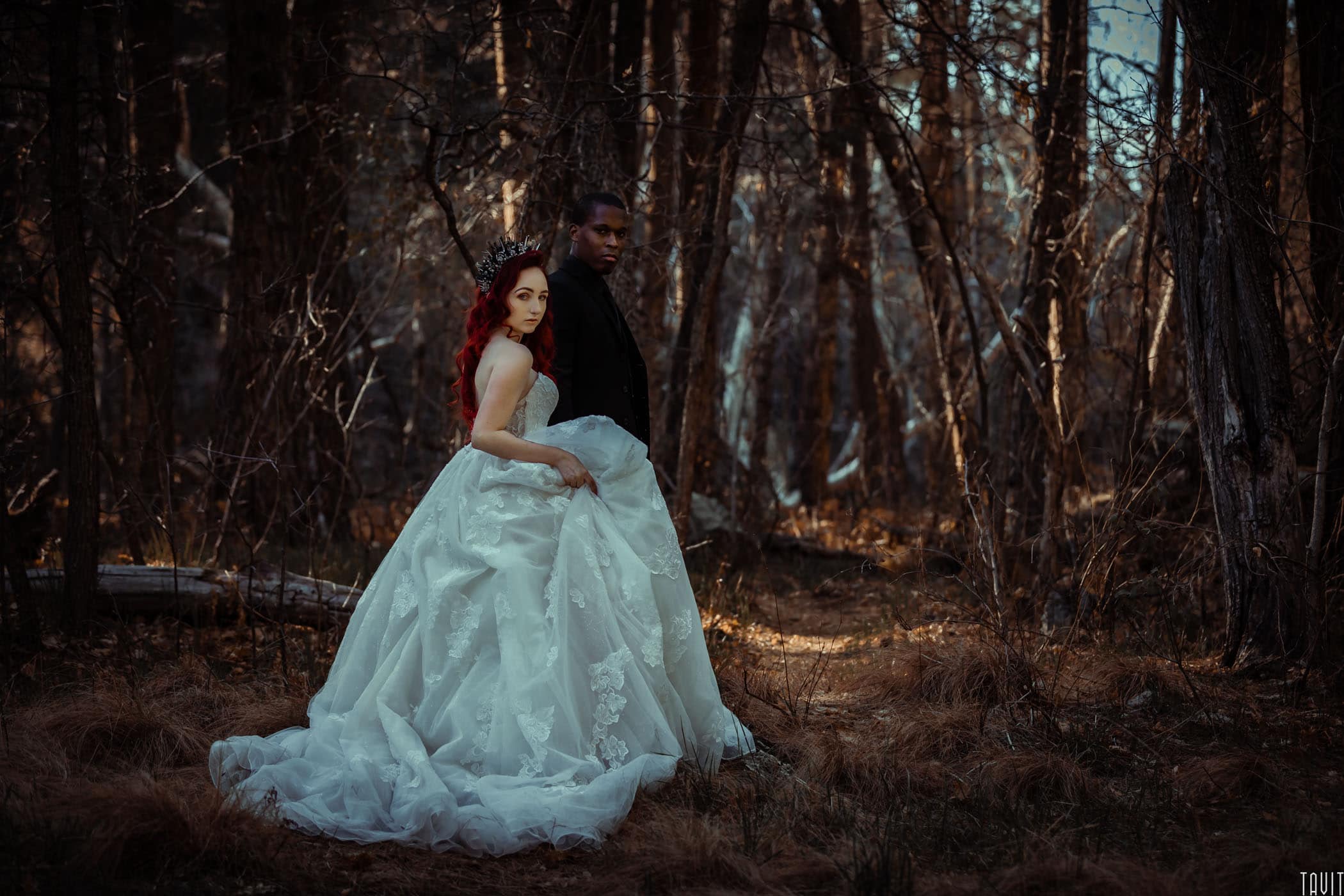 Bride holding dress with groom in forest
