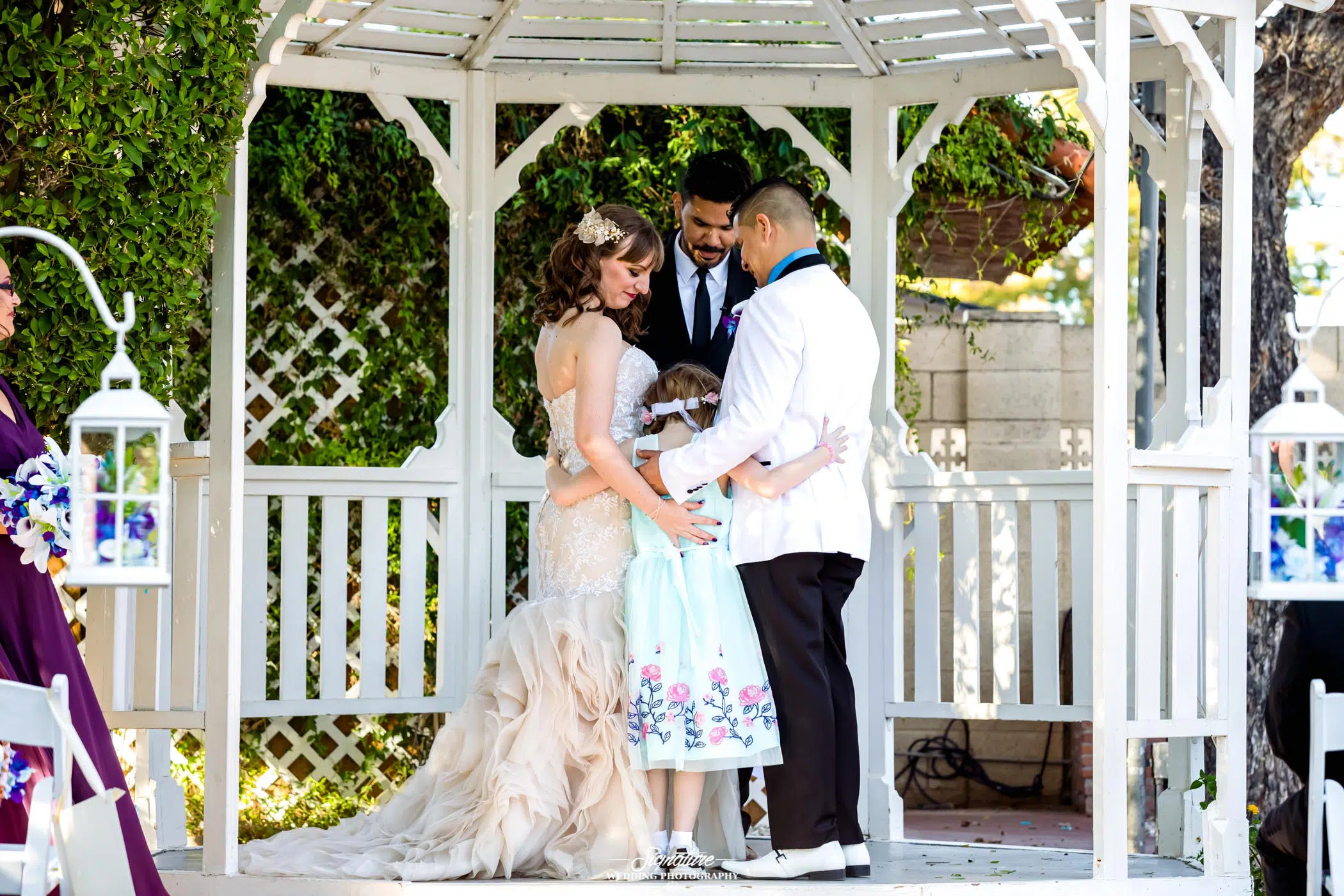 Bride and groom hugging looking down at child during ceremony