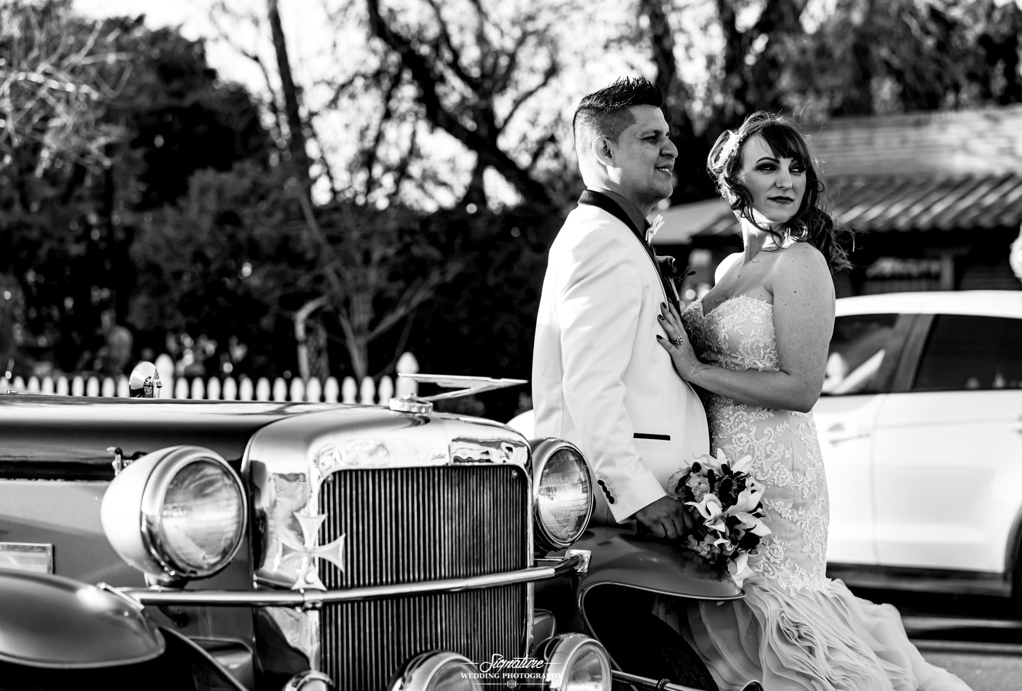 Bride and groom looking over shoulder in front of vintage car black and white