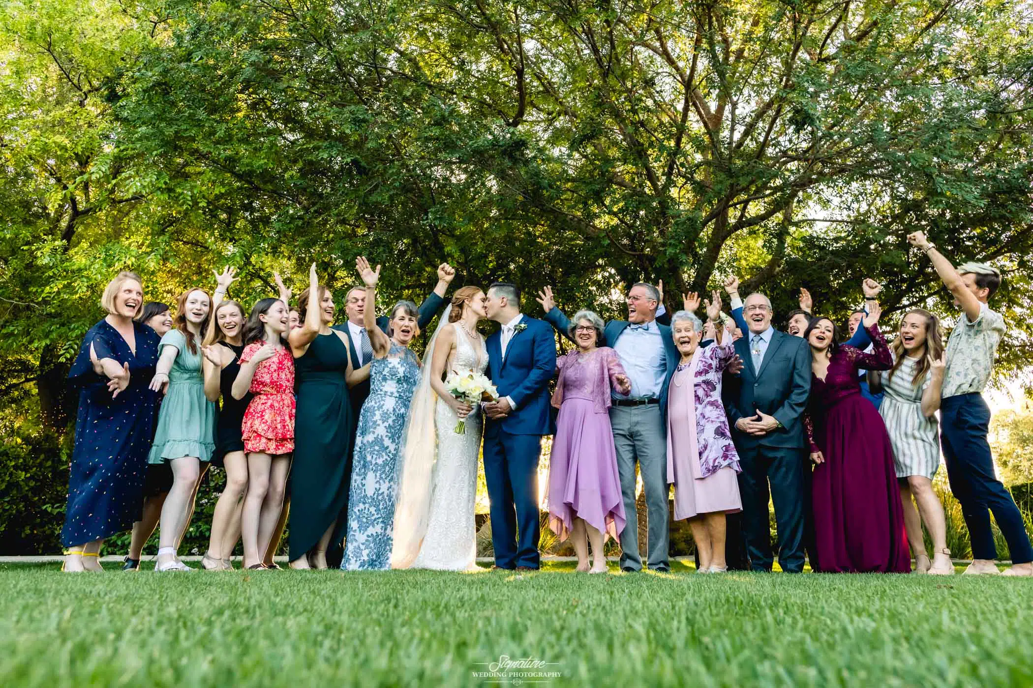 Bride and groom kiss with whole family celebrating