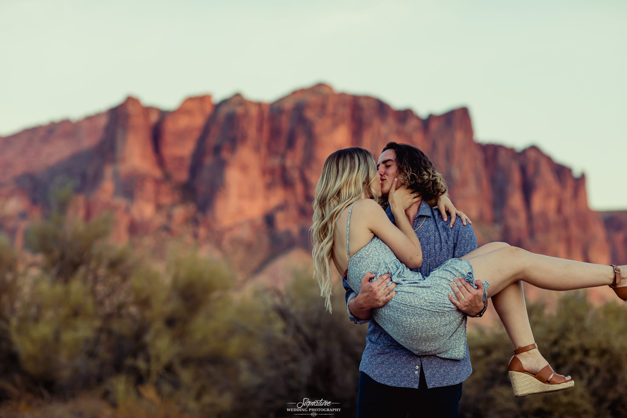 Guy holding girl in arms and kissing in desert