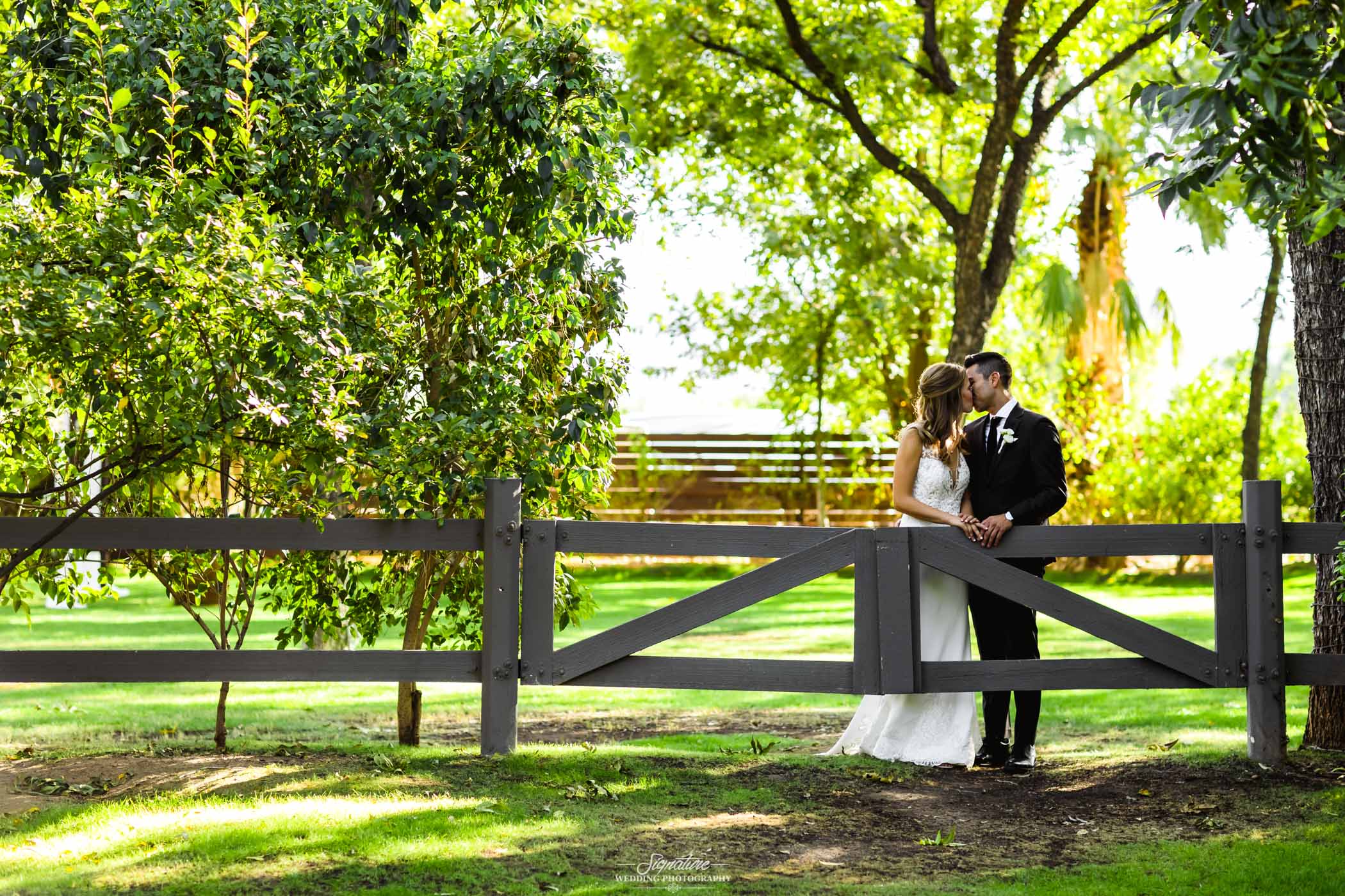 Bride and groom kissing behind fence gate with trees