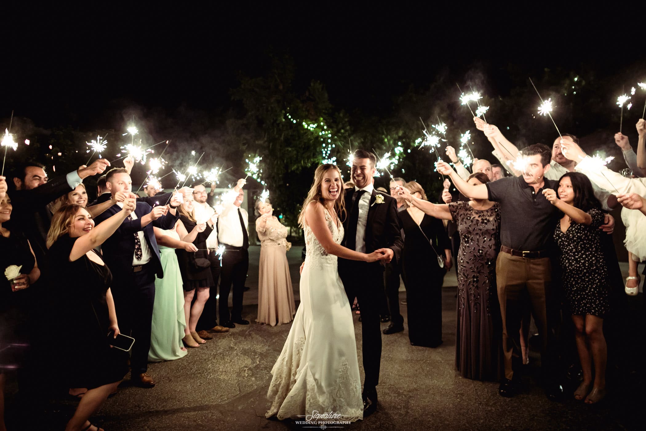 Bride and groom surrounded with wedding guests holding sparklers