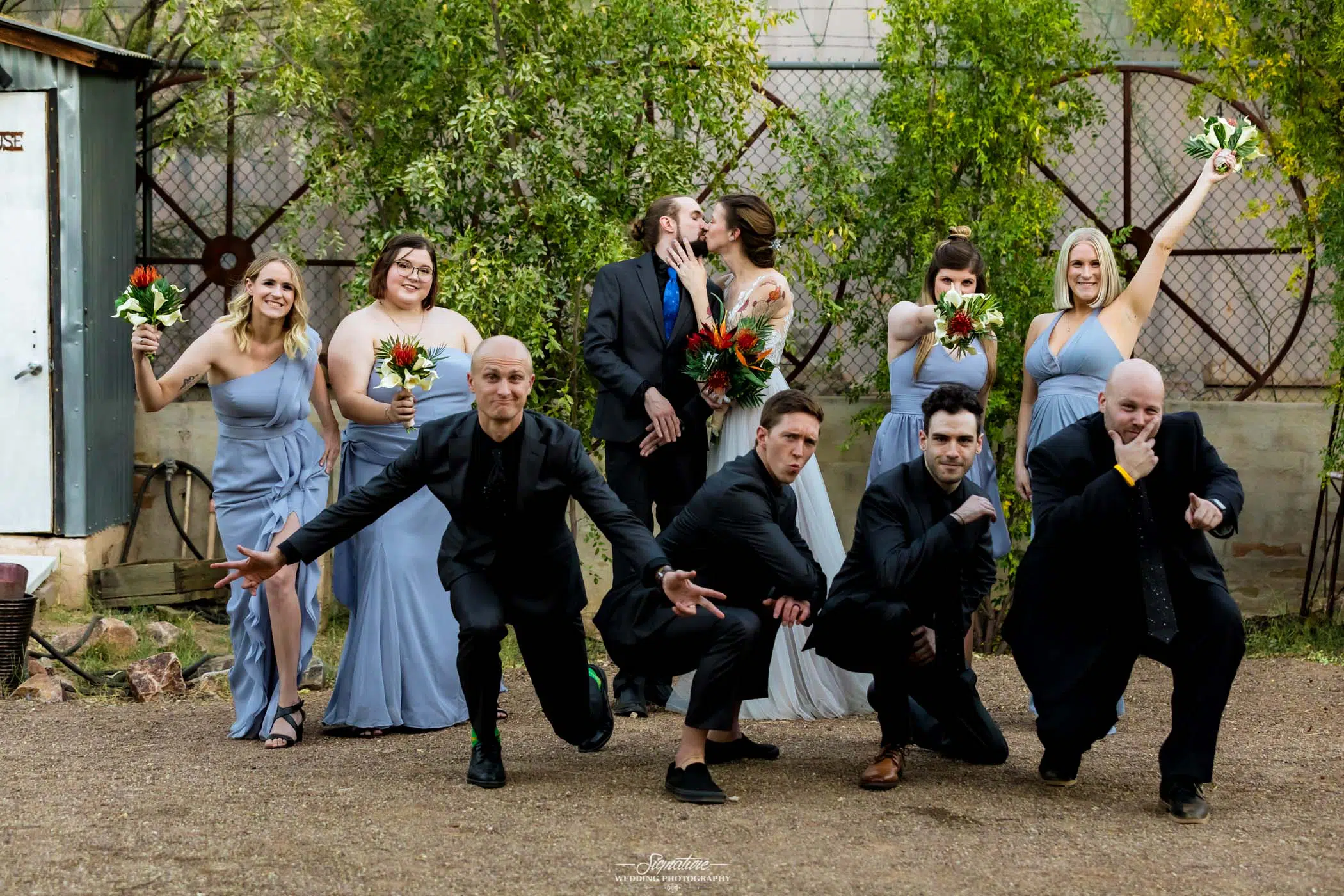 Bride and groom kissing white wedding party poses around them