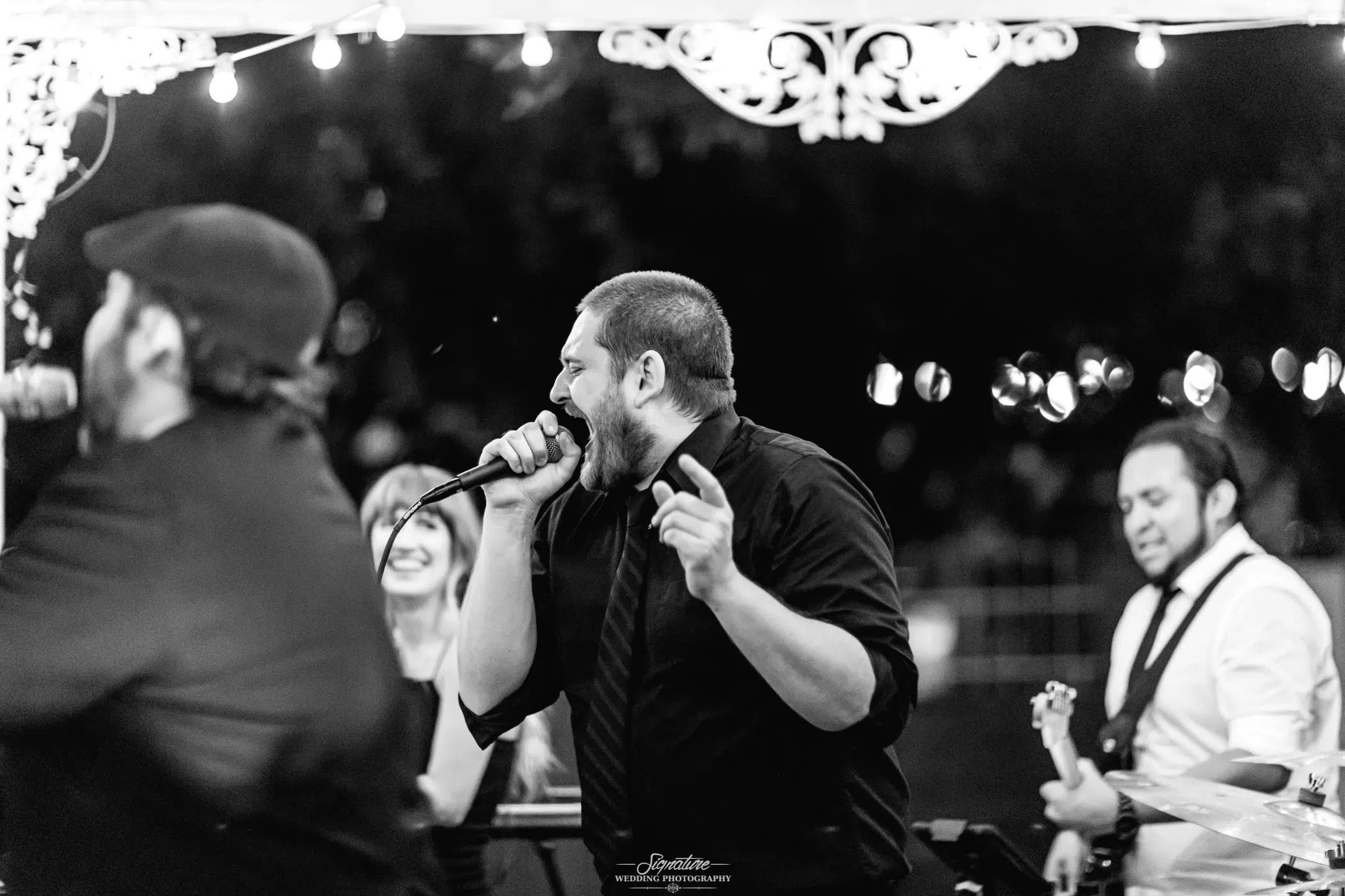 Man singing into mic with band black and white
