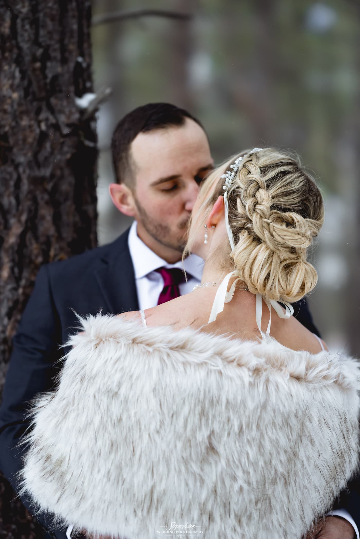 Bride and groom kissing next to tree