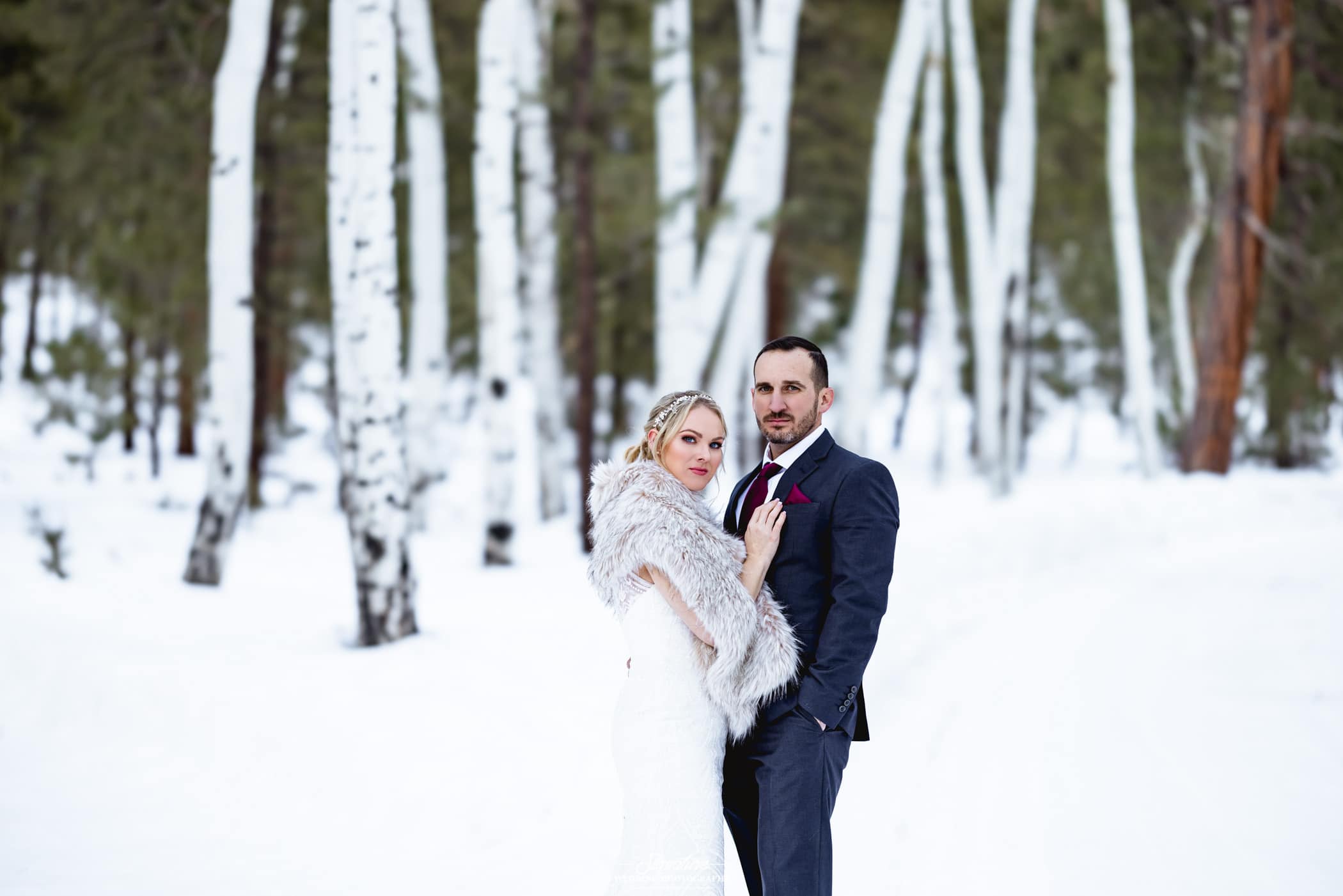 Bride and groom posing for camera in front of winter forest