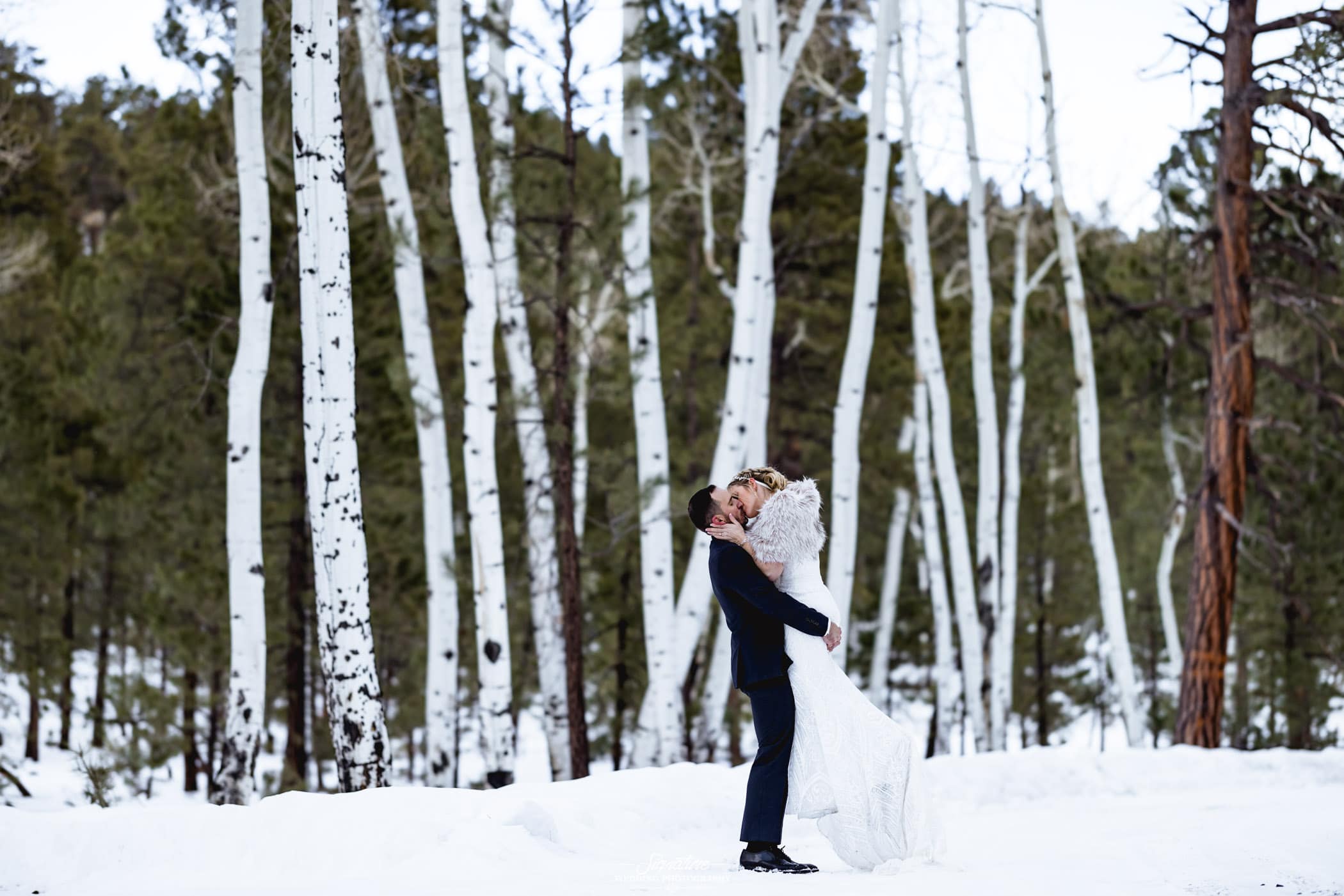 Groom picking up bride and kissing in forest with snow