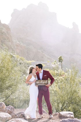 Bride and kissing with elopement sign in desert