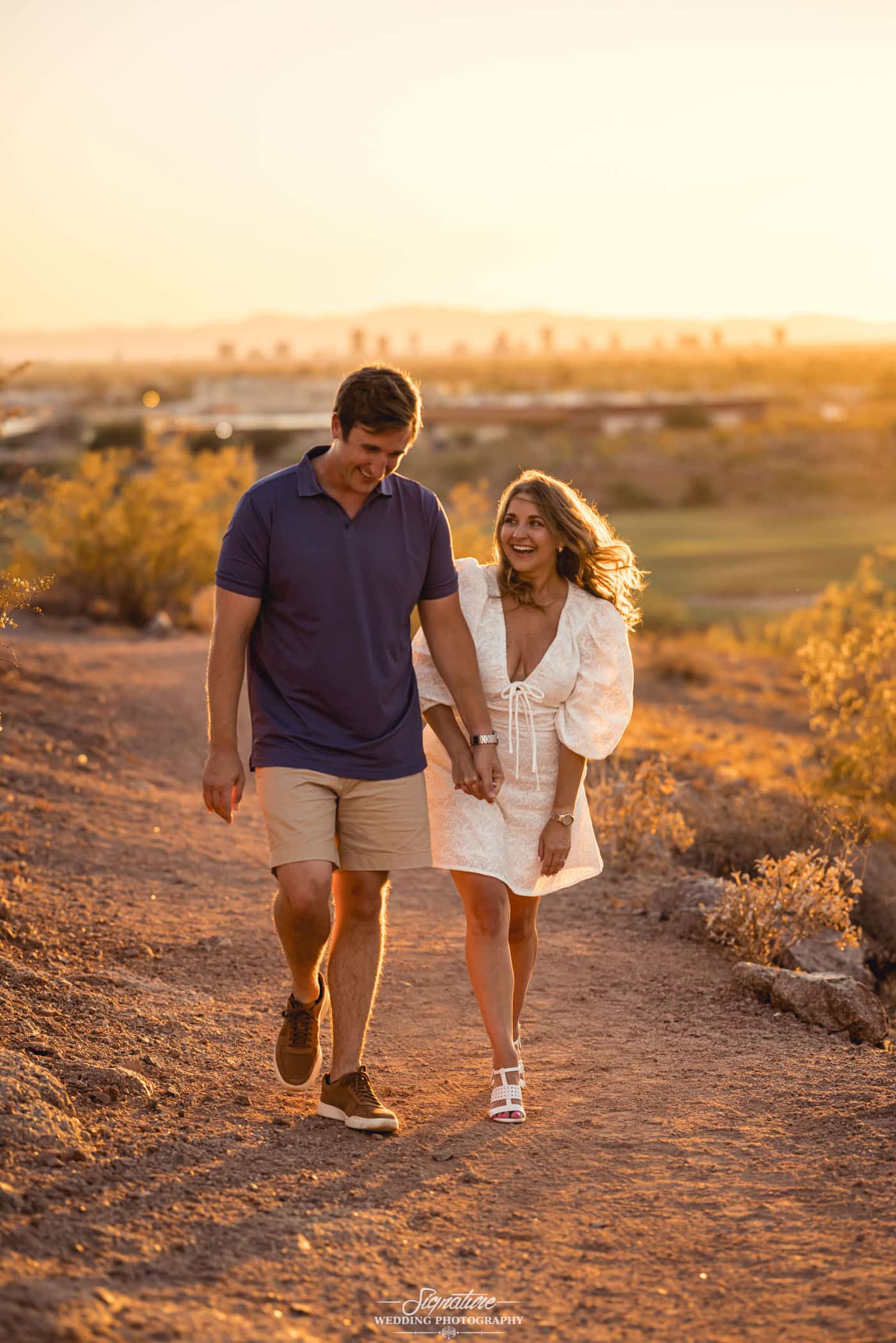 Engaged couple holding hands walking on desert path