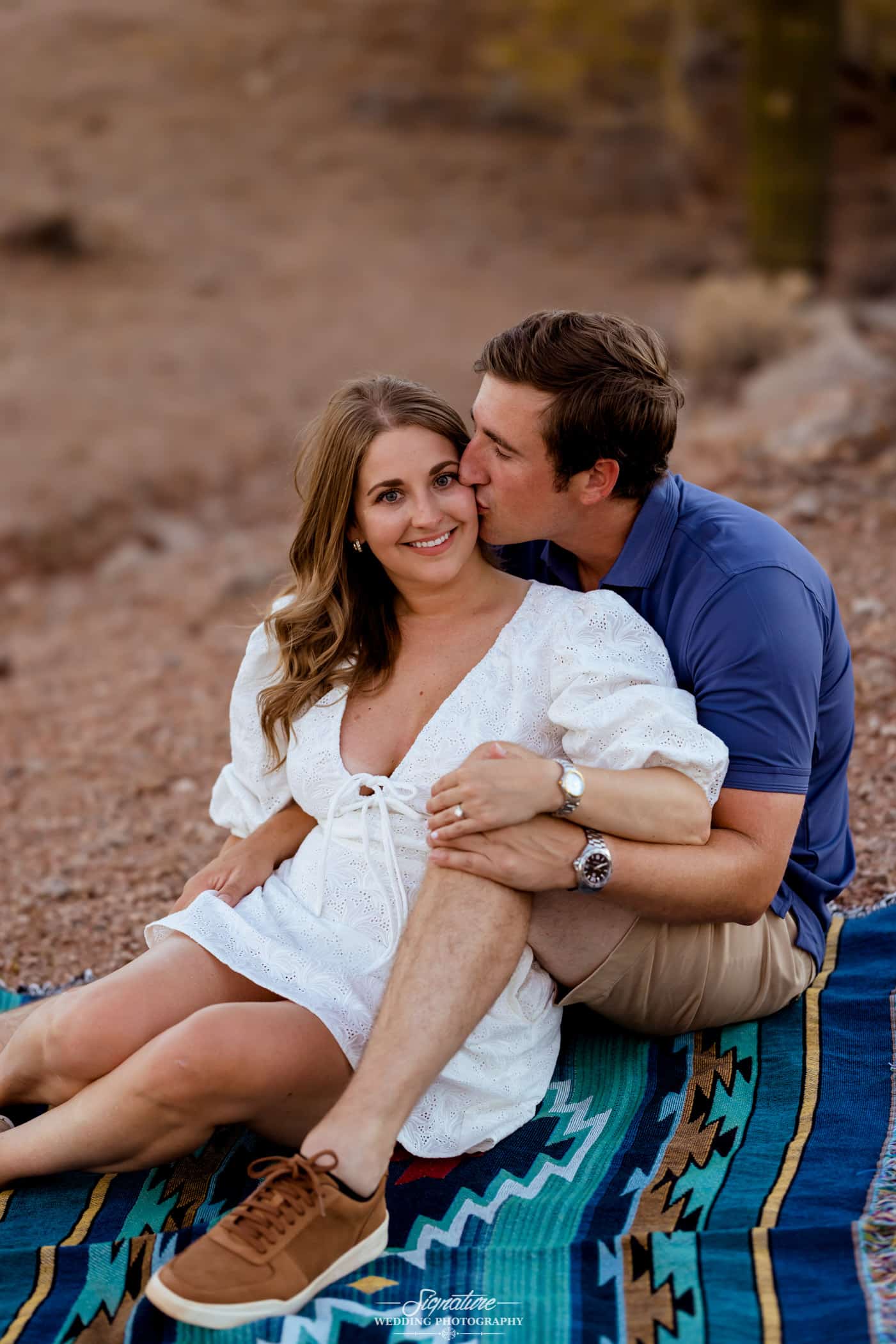 Man kissing woman's cheek sitting on blanket in desert