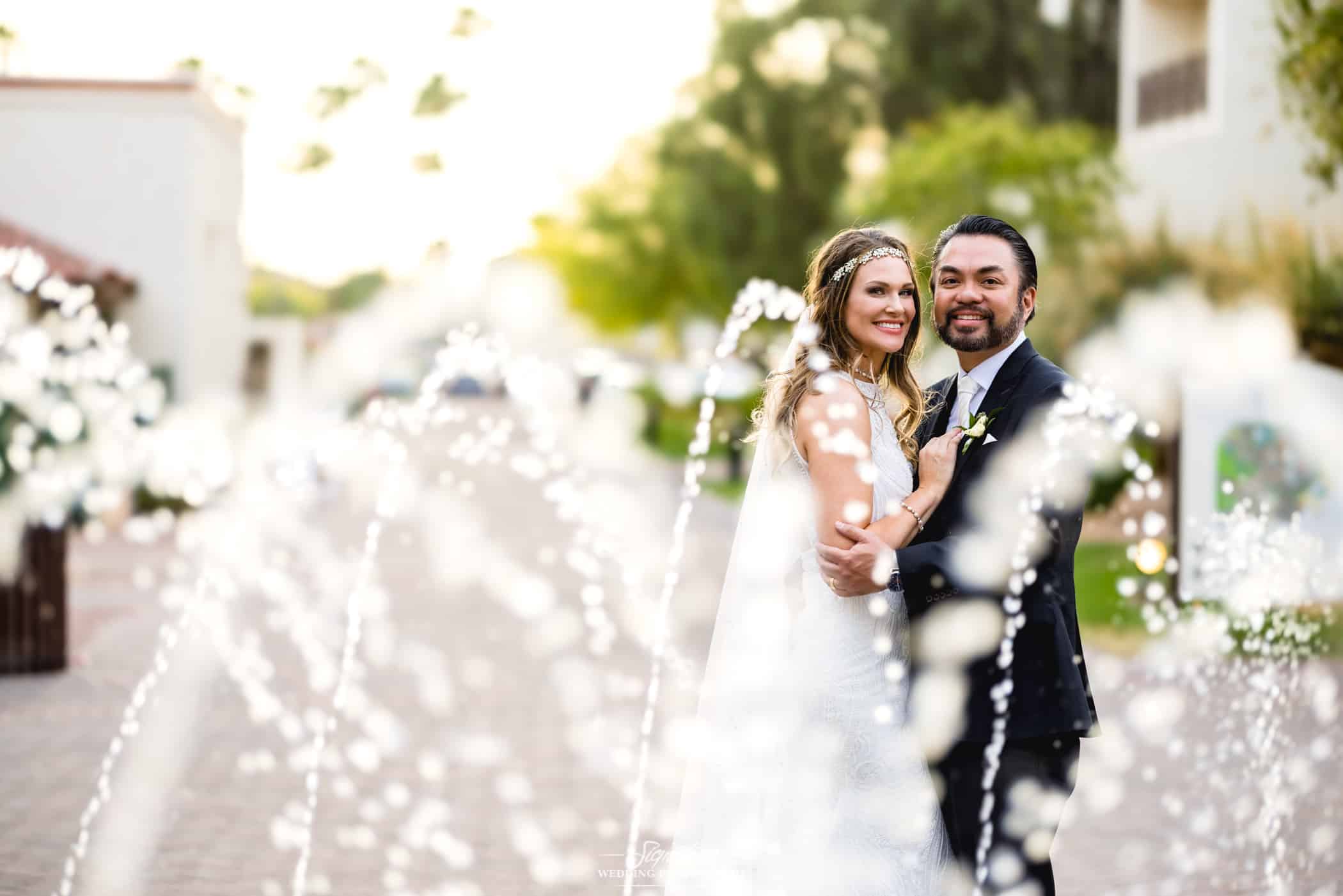 Bride and groom smiling behind water fountain