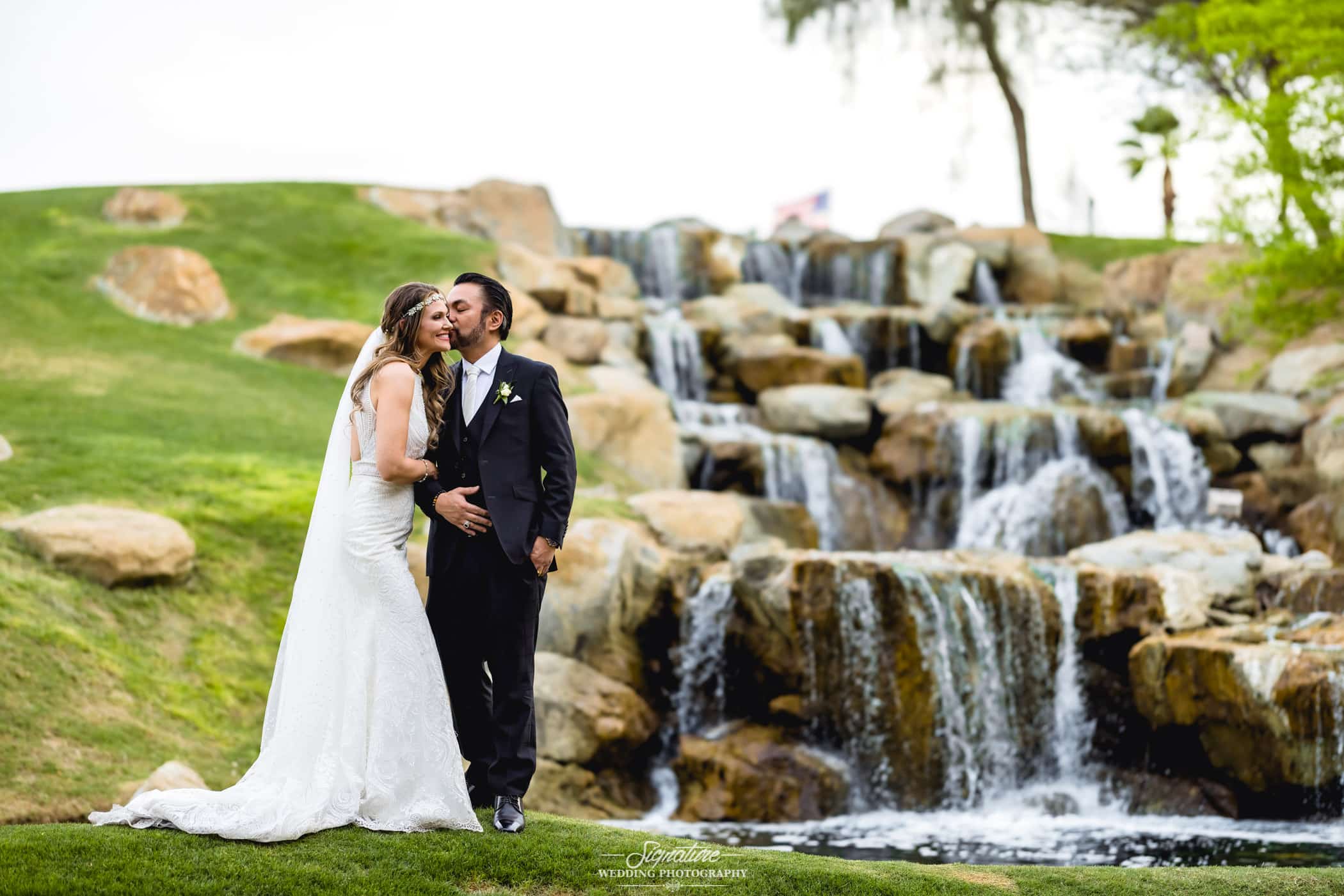 Groom kissing bride's cheek next to waterfall