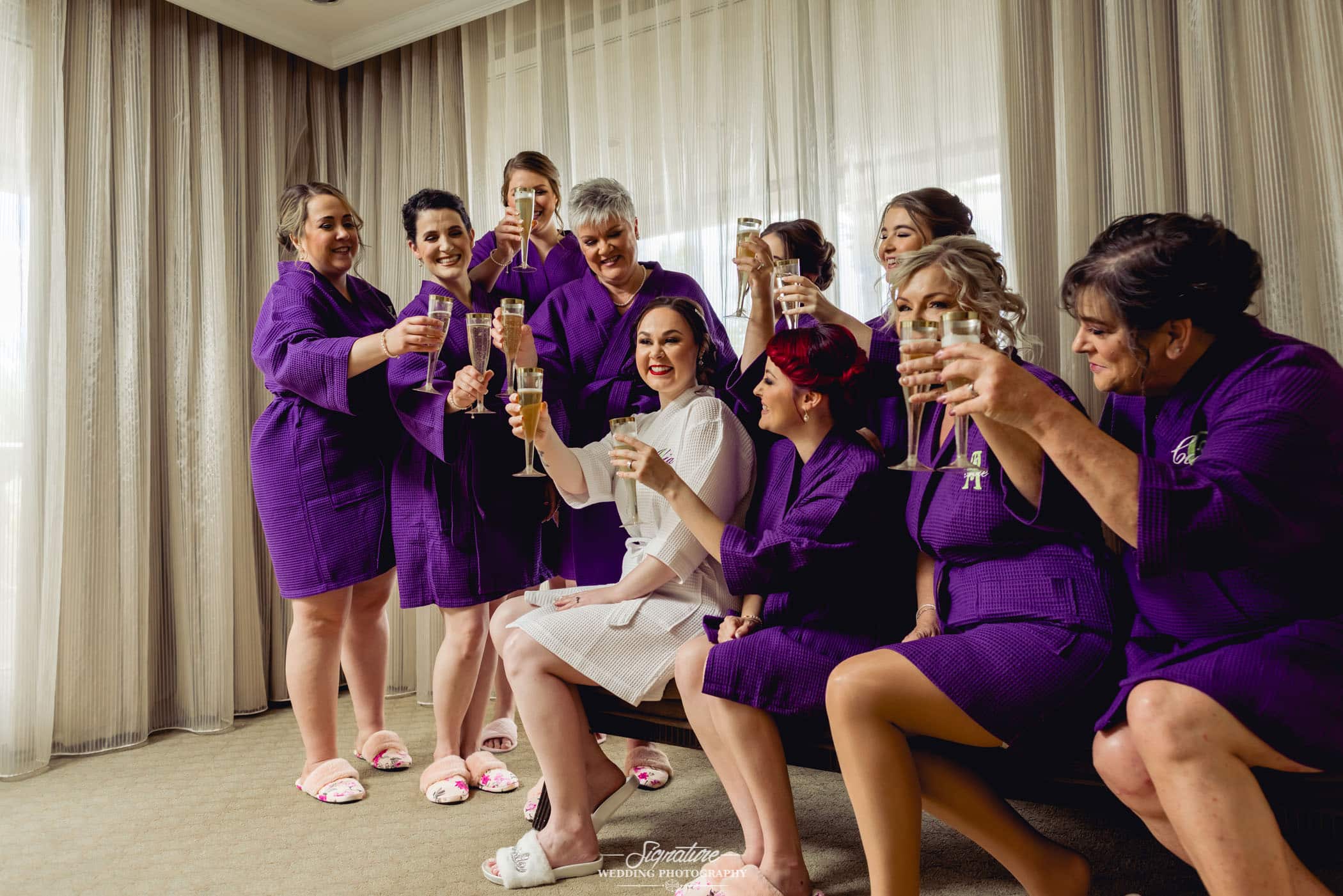 Bride raising at toast with bridesmaids in robes getting ready